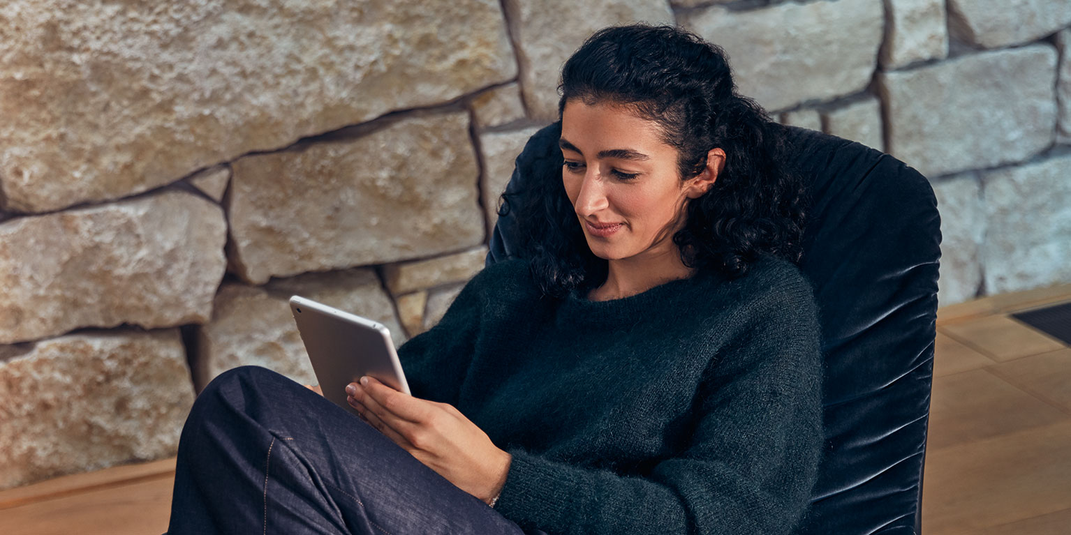 Mantente conectado con la tecnología moderna Persona descansando con una tablet en una silla delante de un muro de piedra