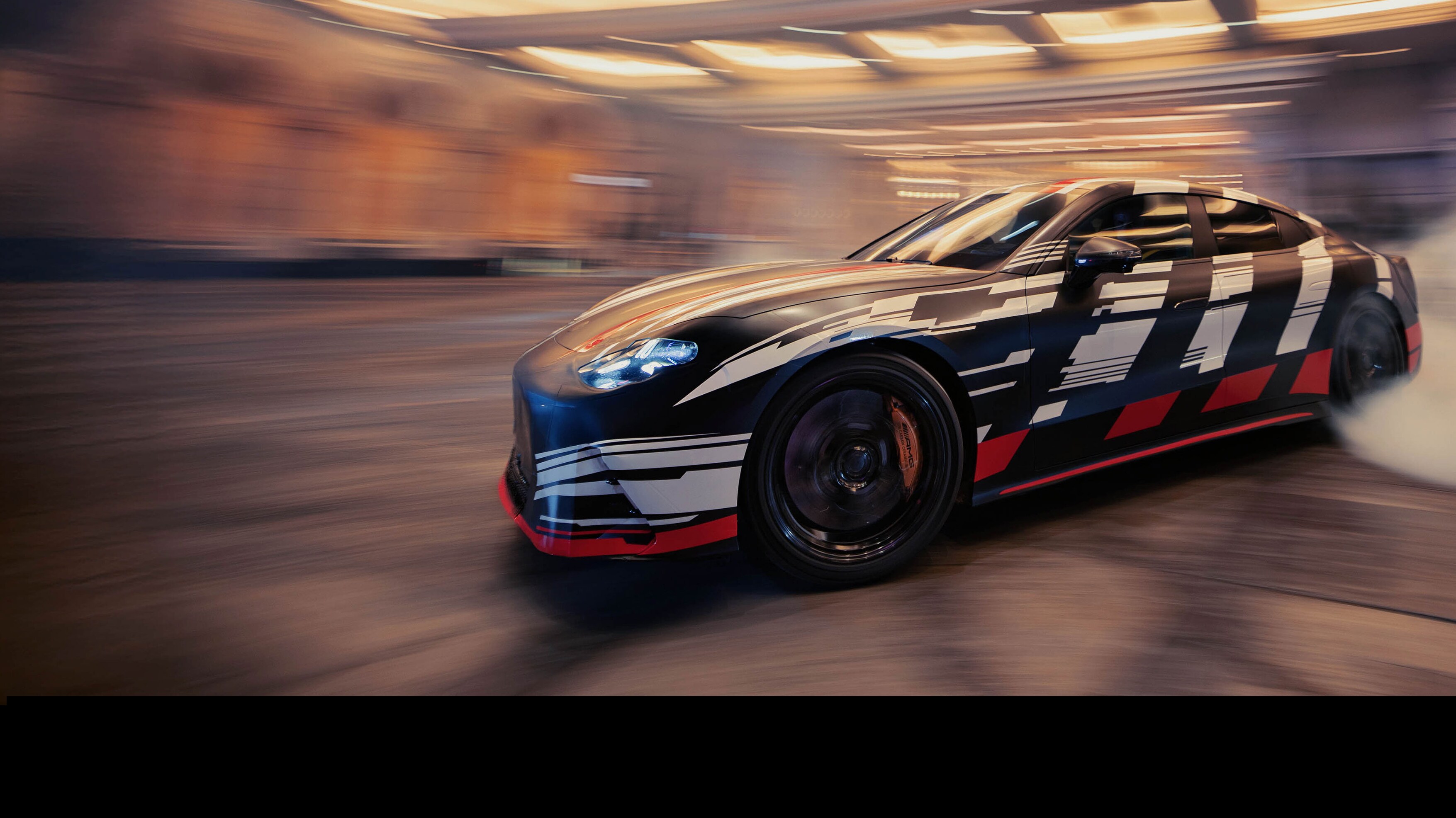 Visual lteral del nuevo Mercedes-AMG GT 4 Puertas Coupé derrapando en el asfalto en color negro con rayas blancas y rojas