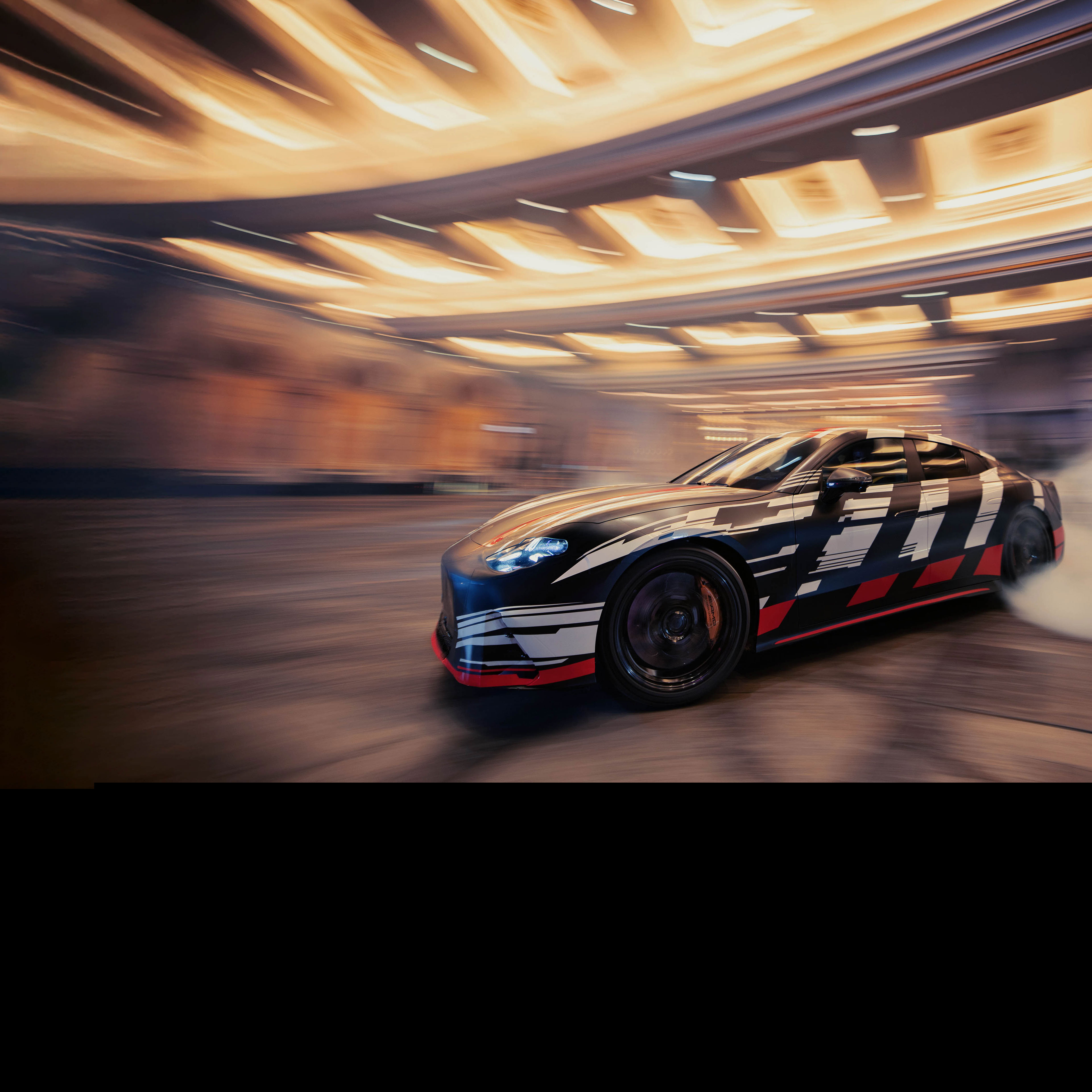 Visual lteral del nuevo Mercedes-AMG GT 4 Puertas Coupé derrapando en el asfalto en color negro con rayas blancas y rojas
