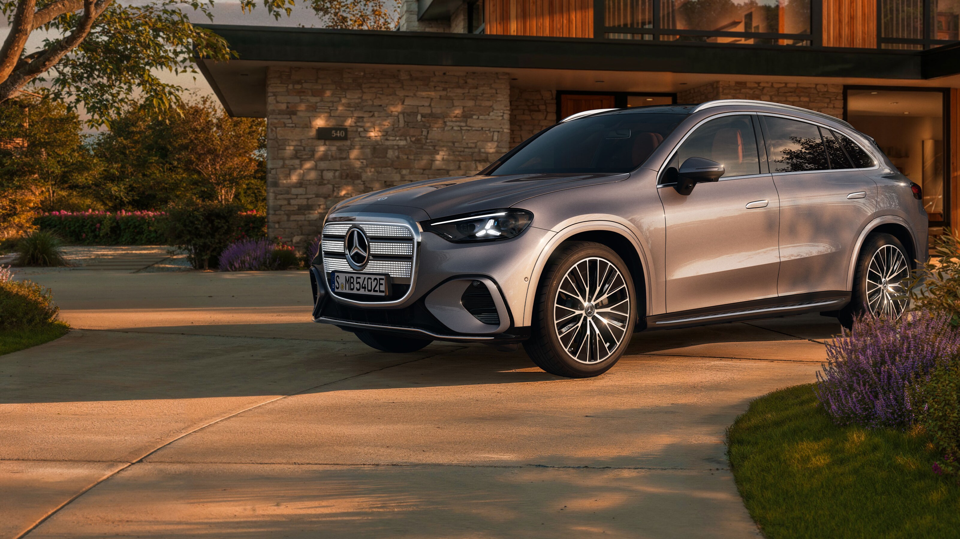 Visual del nuevo GLC eléctrico en color gris de Mercedes-Benz aparcado fuera de una casa