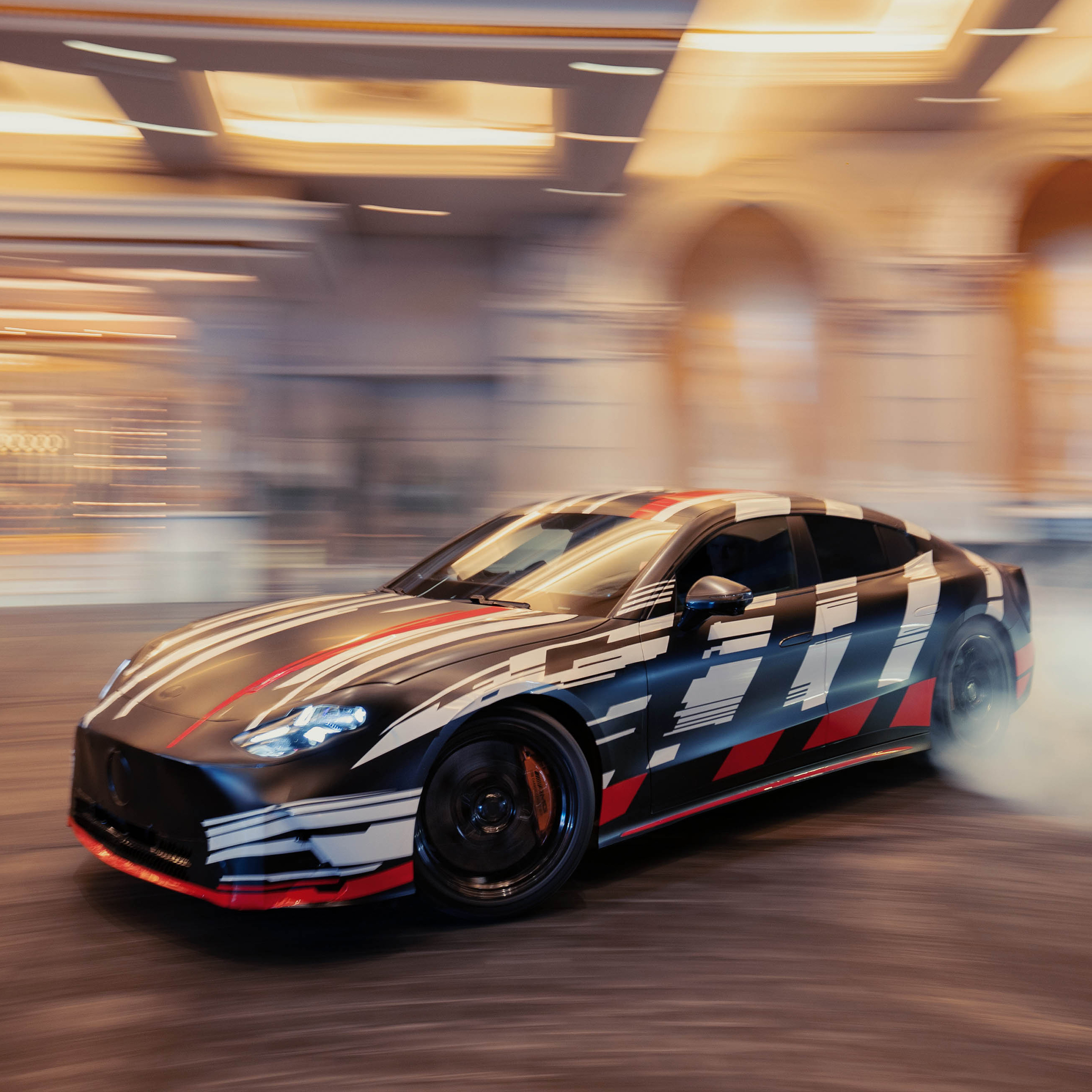 Presentación mundial en directo | GT 4 Puertas Coupé | Mercedes-AMG Visual lateral del nuevo Mercedes-AMG GT 4 Puertas Coupé en color negro con rayas blancas y rojas derrapanado en una pista