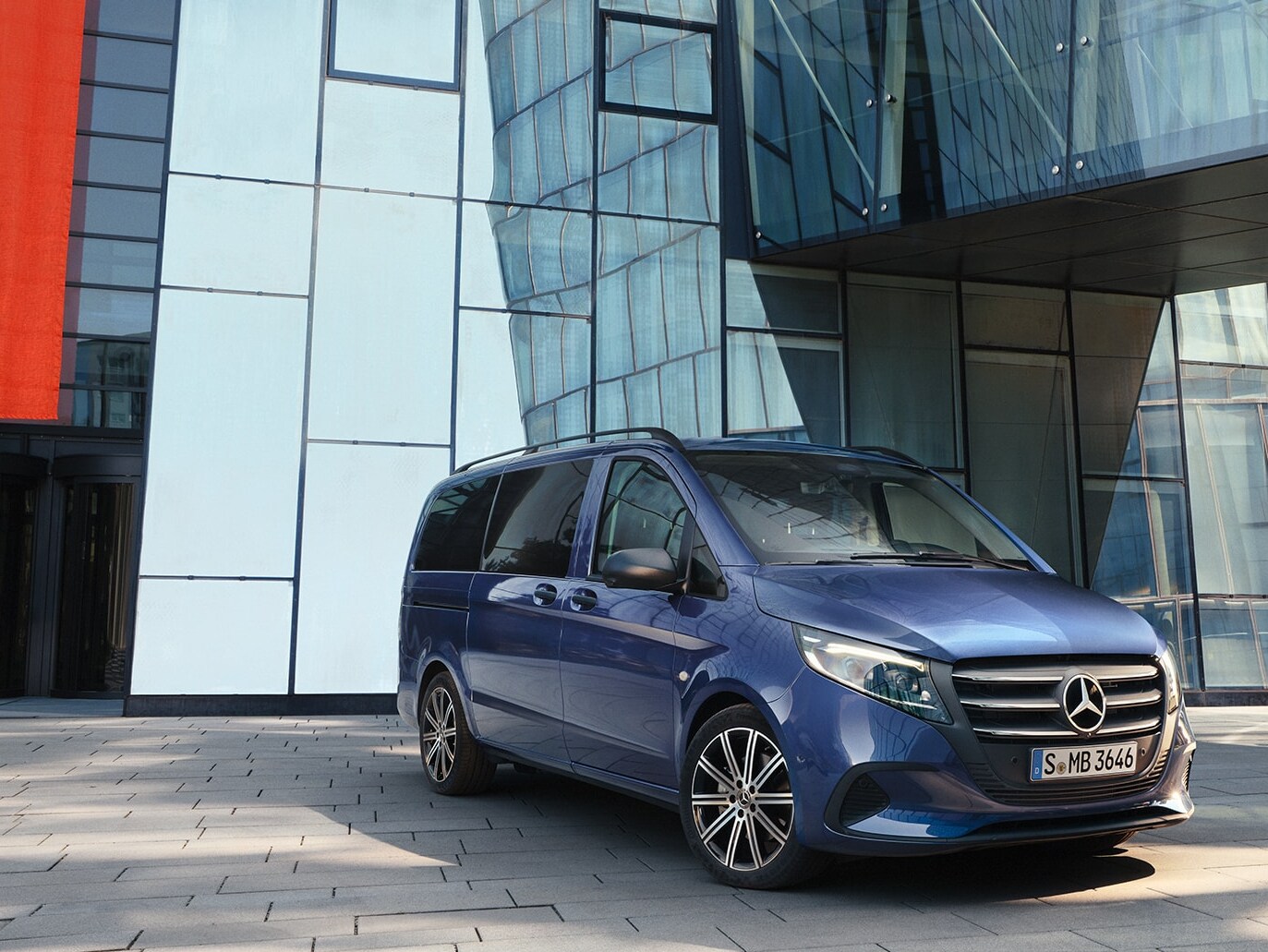 Una Vito Tourer de Mercedes-Benz con puerta corredera frente a un edificio moderno.