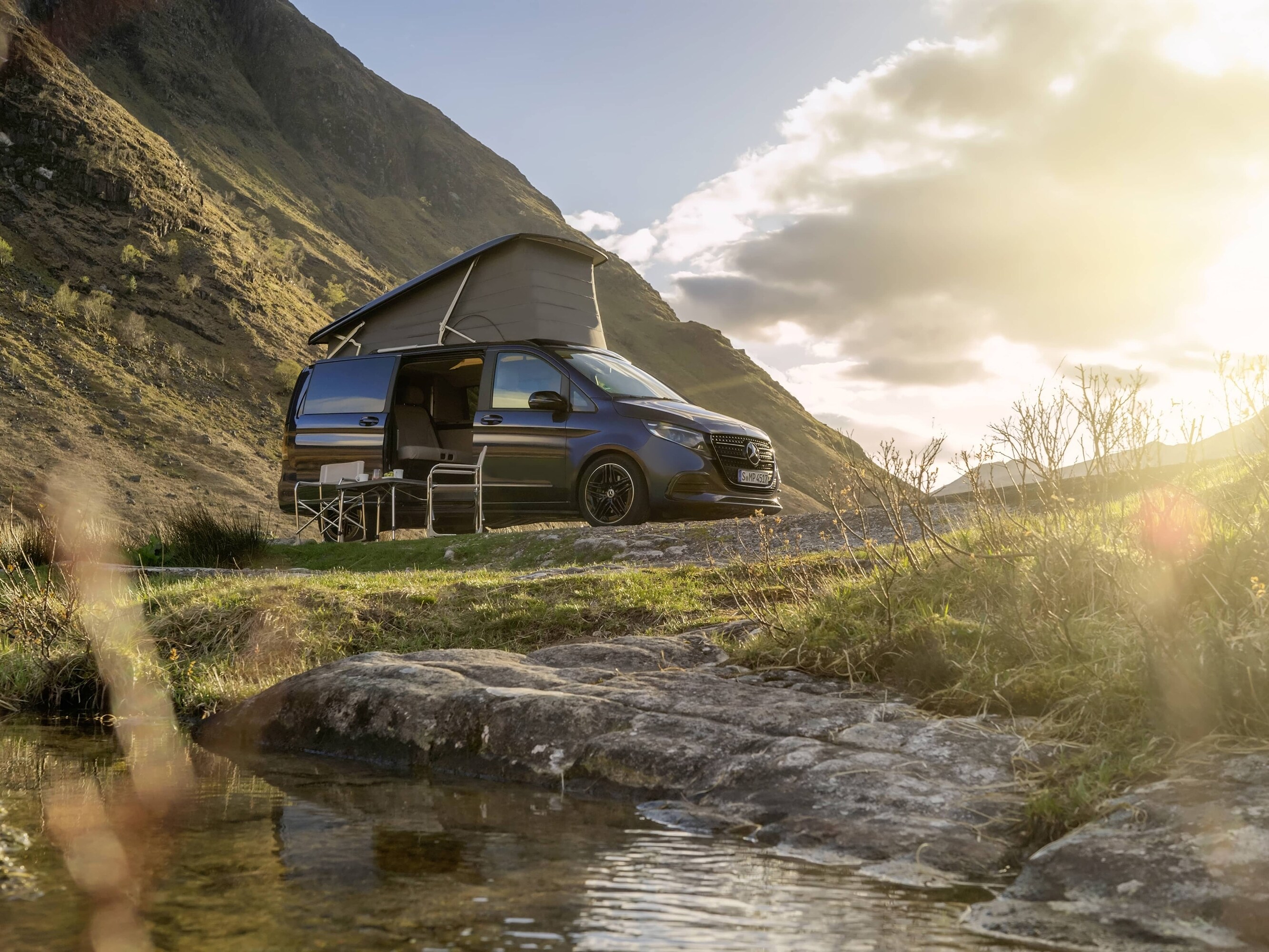 Una autocaravana Mercedes-Benz Marco Polo con techo elevable, situada en un pintoresco paisaje montañoso, que muestra la aventura al aire libre y la libertad de la «vida en autocaravana».