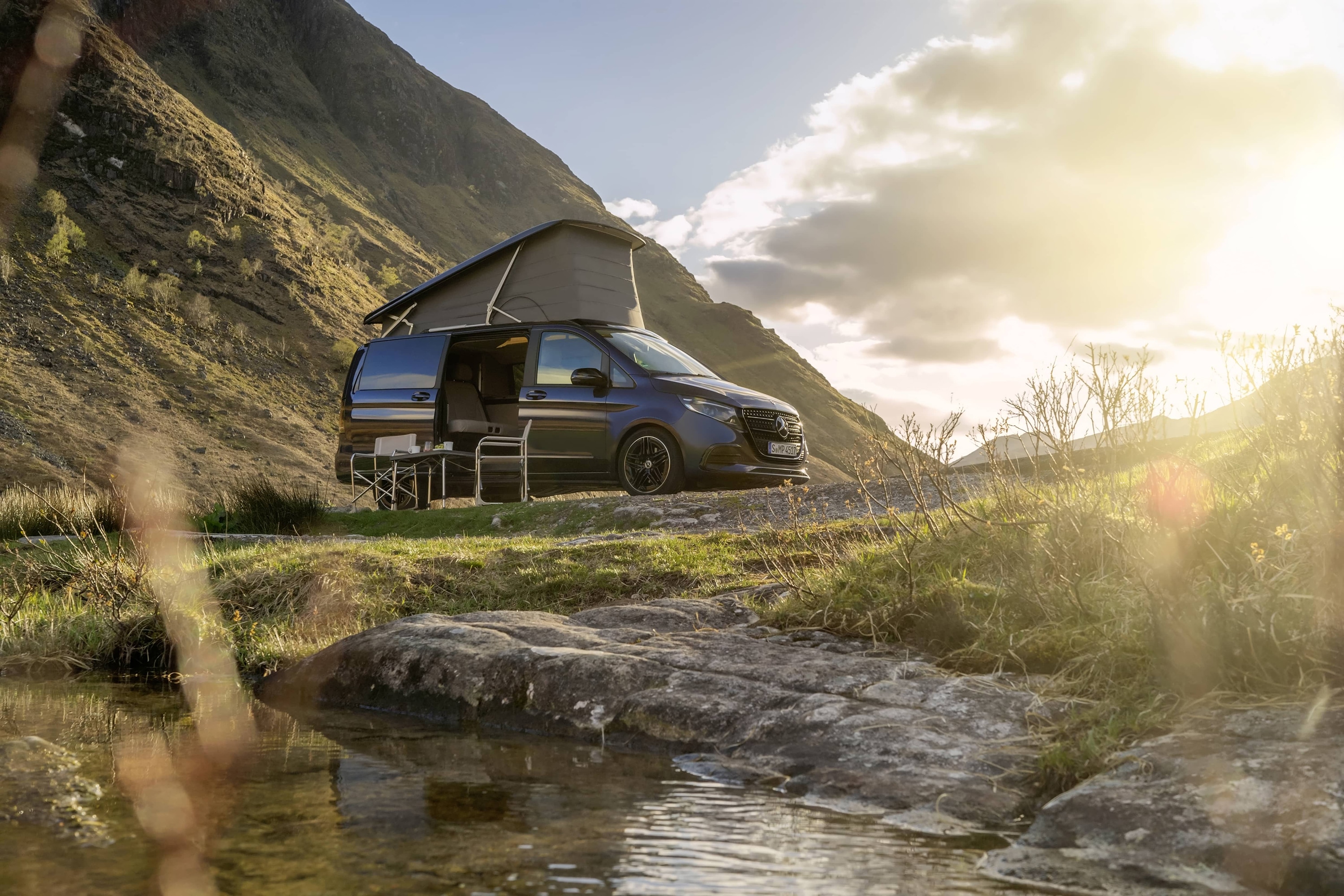 Marco Polo | Autocaravanas Sprinter | Mercedes-Benz Una autocaravana Mercedes-Benz Marco Polo con techo elevable, situada en un pintoresco paisaje montañoso, que muestra la aventura al aire libre y la libertad de la «vida en autocaravana».