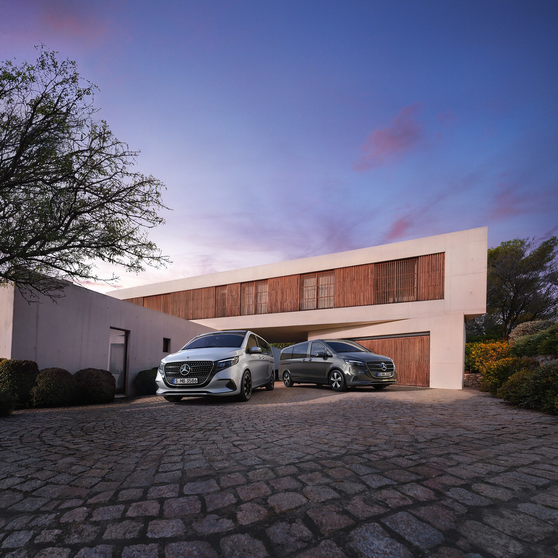 Una Mercedes-Benz Clase V frente a una vivienda moderna y lujosa al atardecer.