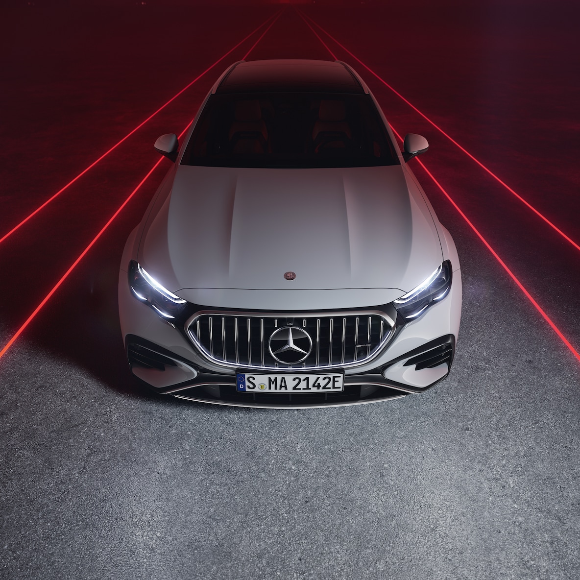 Vista frontal del Mercedes-AMG E 53 HYBRID 4MATIC+ sobre fondo rojo visto desde arriba.