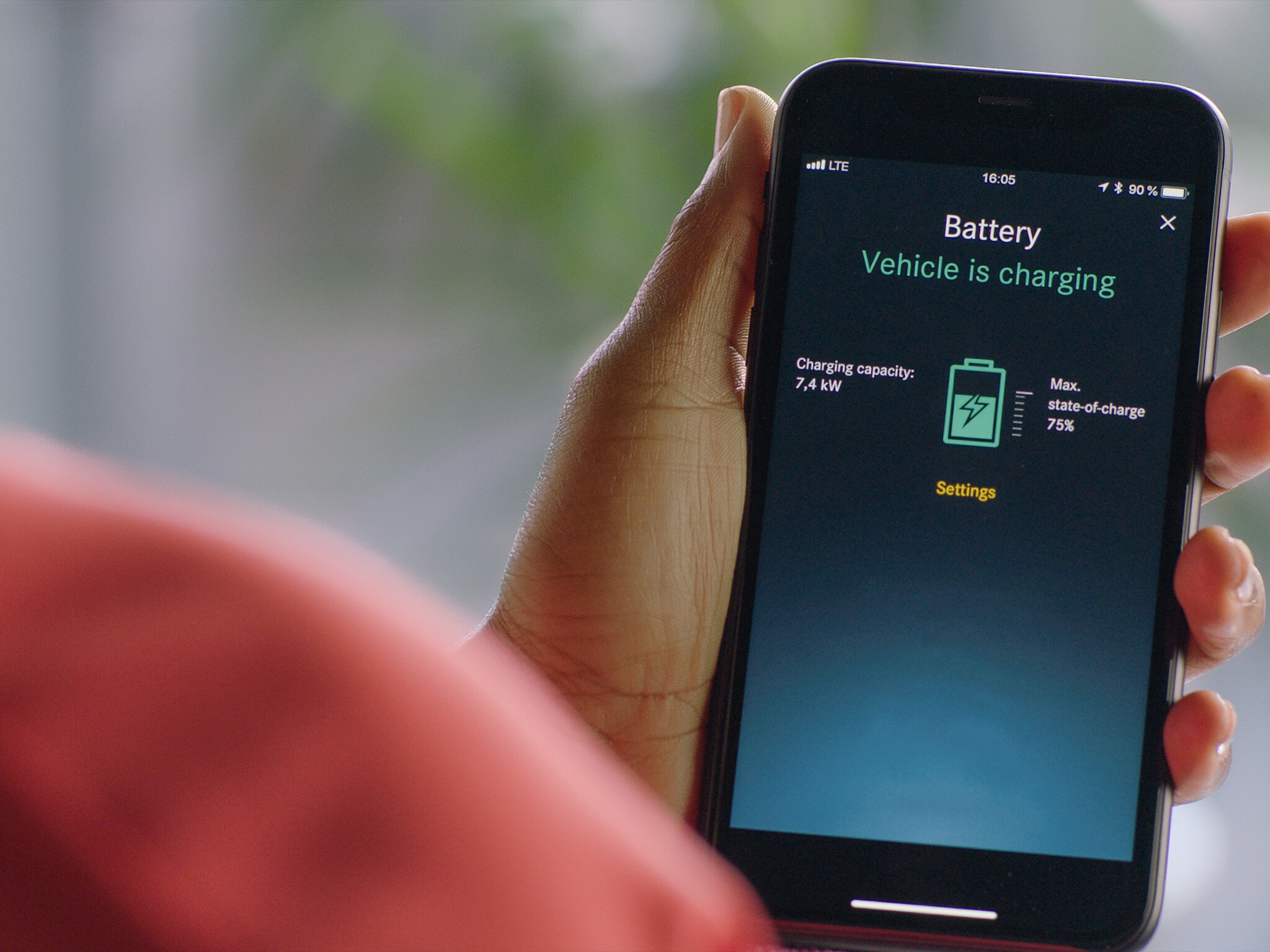 Una mano sosteniendo un smartphone para comprobar el proceso de carga de un vehículo eléctrico