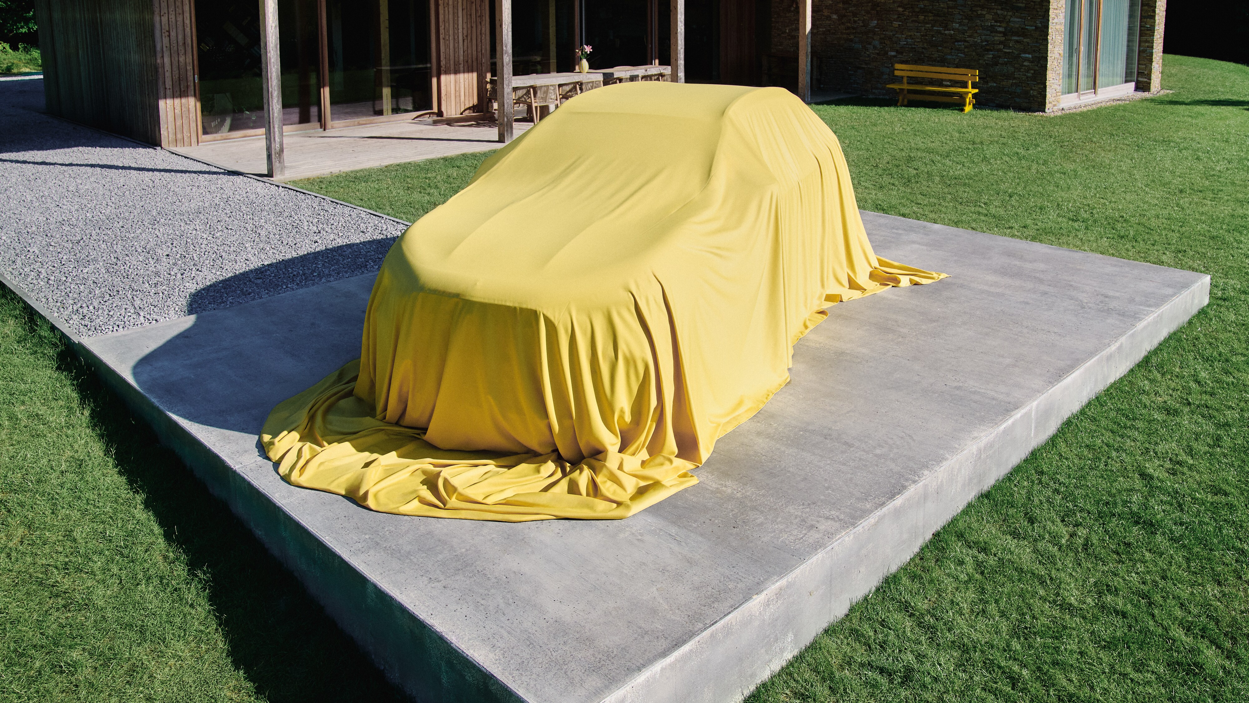 Visual del nuevo GLA cubierto con un velo amarillo frente a una casa.