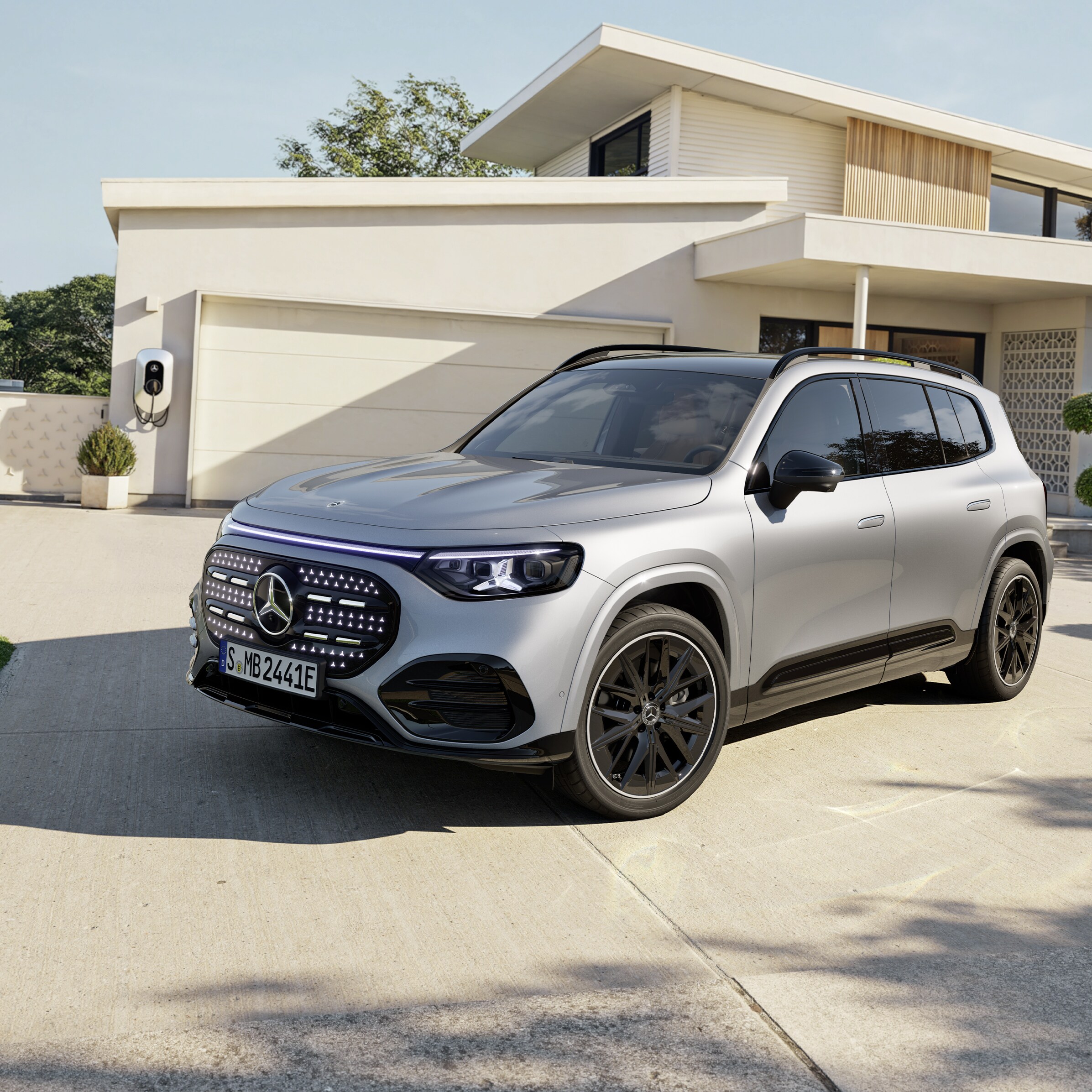 Visual lateral frontal de un GLB gris de Mercedes-Benz aparcado fuera de una casa con un cargador eléctrico instalado