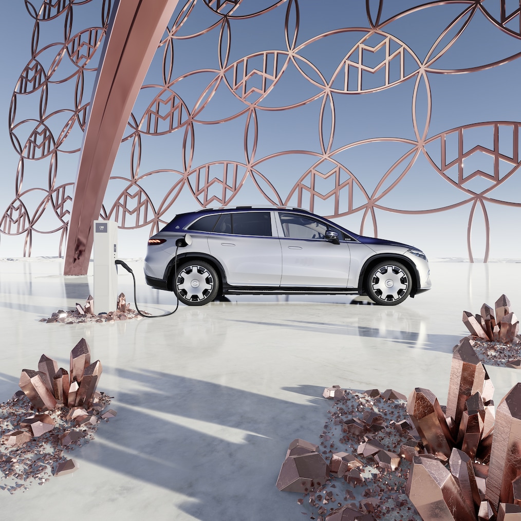 Vista lateral del Mercedes-Maybach EQS SUV en la estación de carga, con el logotipo de marca Maybach de fondo.