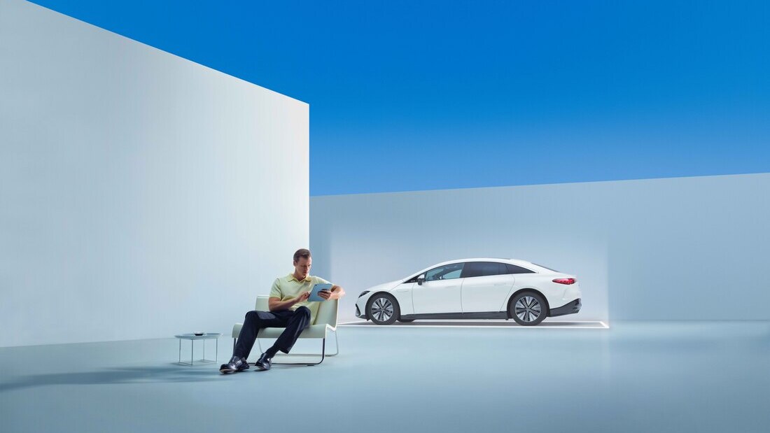 Un hombre sentado delante de un Mercedes-Benz eléctrico con una tablet.