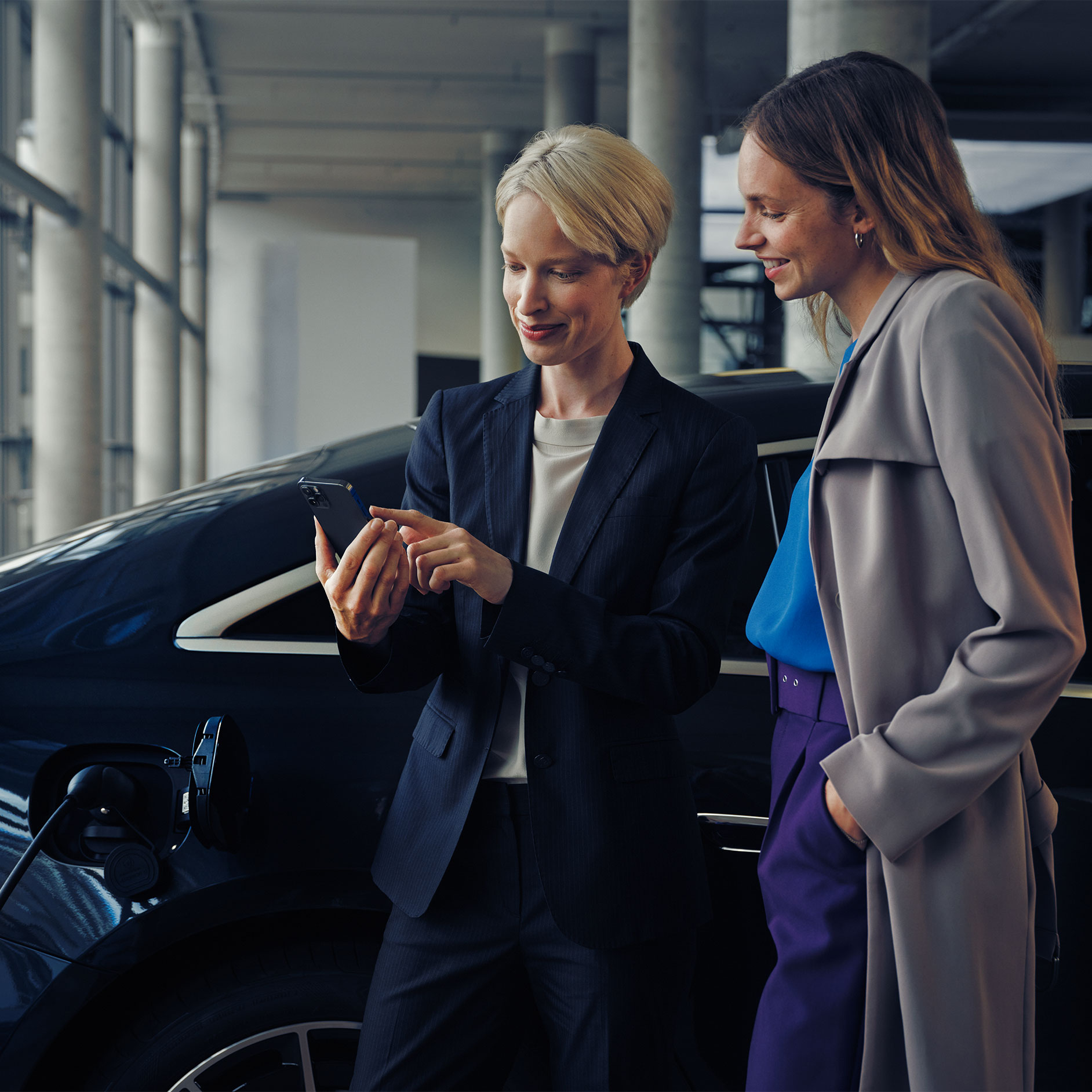 Consulta de instalación | Carga | Mercedes-Benz Dos mujeres delante de una EQE berlina que está siendo cargada.