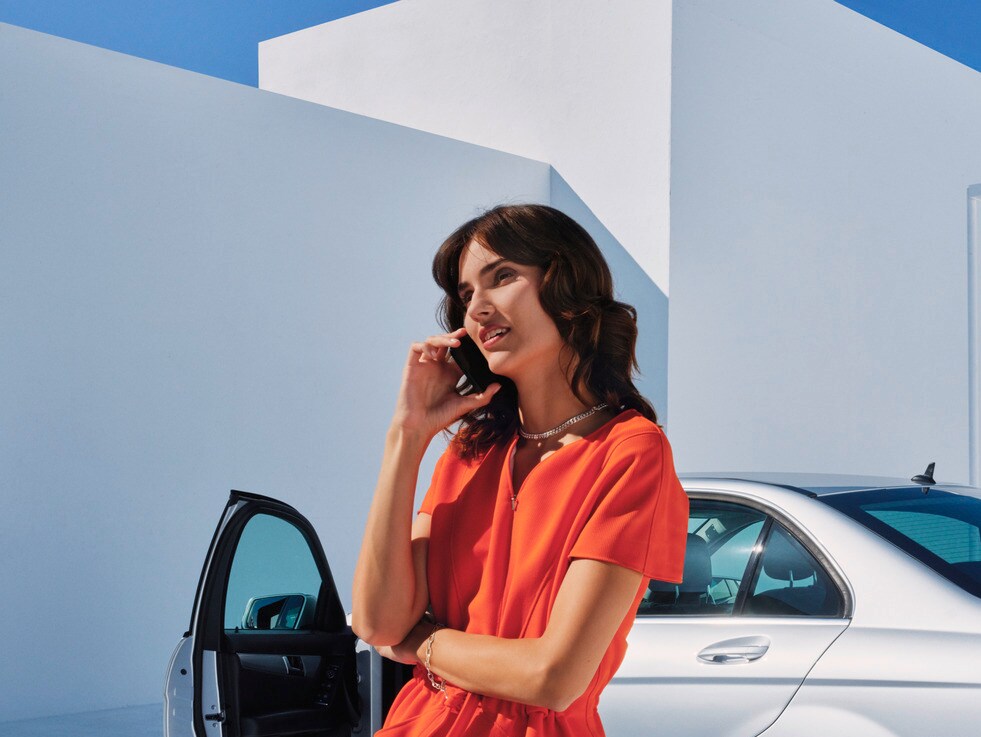 Mujer hablando por teléfono delante de su Mercedes