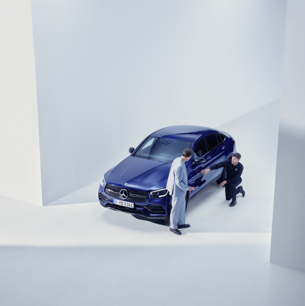 Un técnico inspeccionando un vehículo Mercedes-Benz y consultando con un cliente.