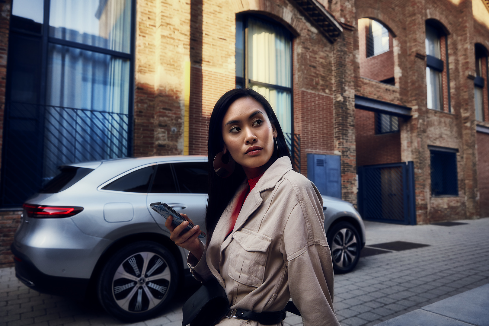 Reserva de hora online | Mercedes-Benz Una mujer se encuentra delante de su Mercedes y sostiene el smartphone en la mano derecha.