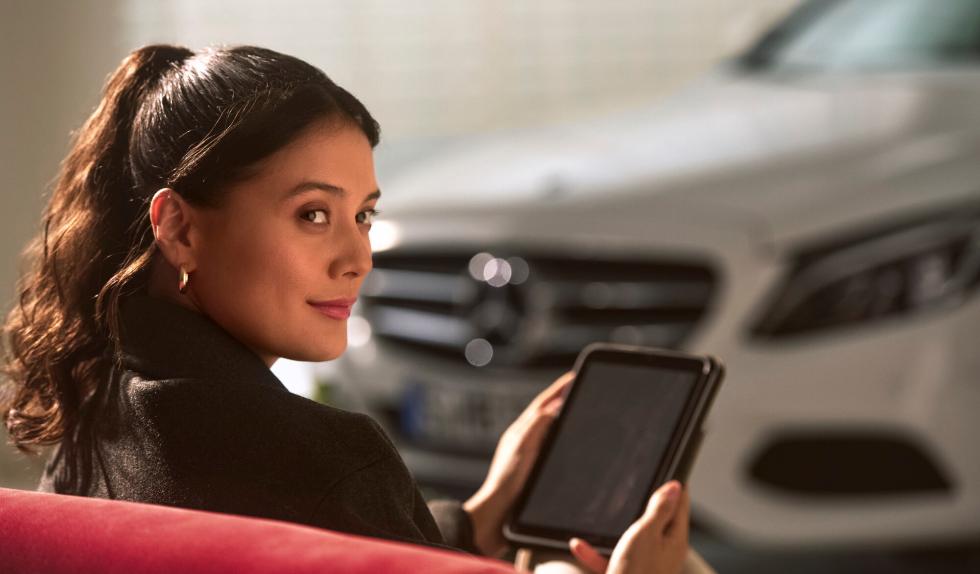 Una persona sentada junto a un vehículo Mercedes-Benz con una tablet en las manos.