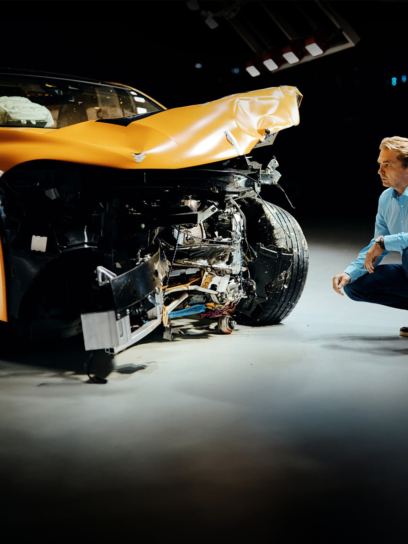 Un experto en pruebas de choque agachado junto a un Mercedes-Benz, examinándolo luego de un impacto frontal.