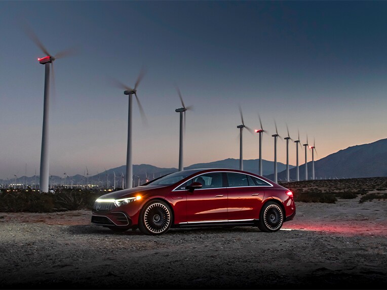 Un Mercedes-Benz EQS rojo (V 297) aparcado delante de unas turbinas eólicas.
