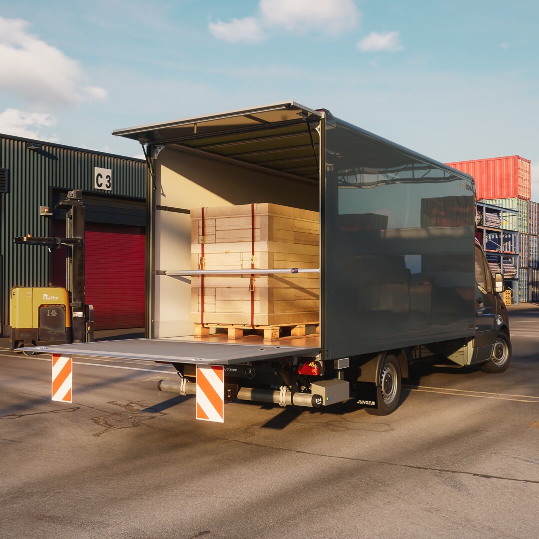 Mercedes-Benz Sprinter con carrocería de caja cerrada para carga seca de Junge durante la carga en un centro logístico: solución de transporte eficiente para carga general y manipulación de mercancías. La puerta trasera abierta muestra paneles de madera paletizados en la zona de carga durante la carga o descarga.