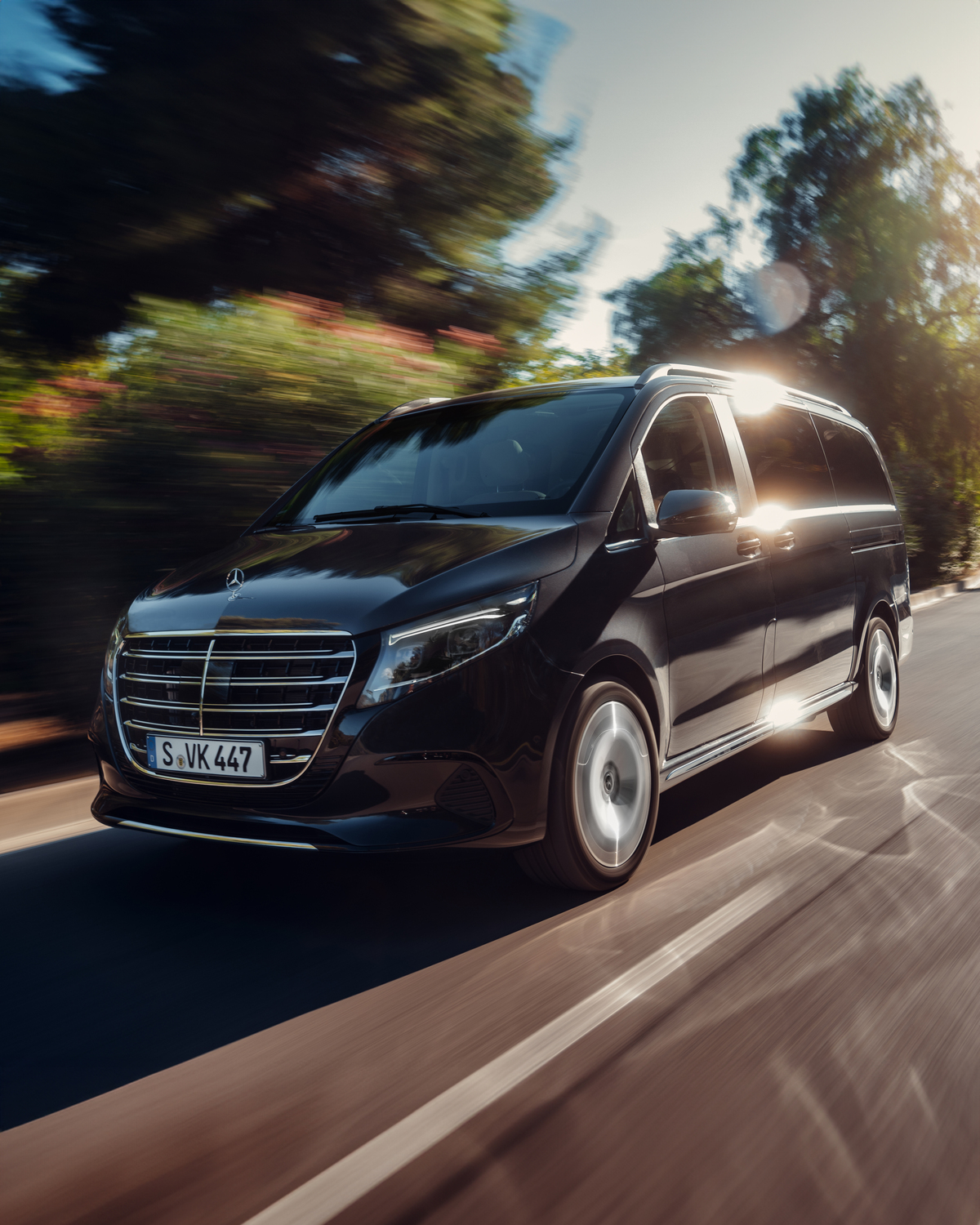 Experimenta la elegancia del Clase V de Mercedes-Benz Mercedes-Benz Clase V negro transitando por un paisaje vibrante
