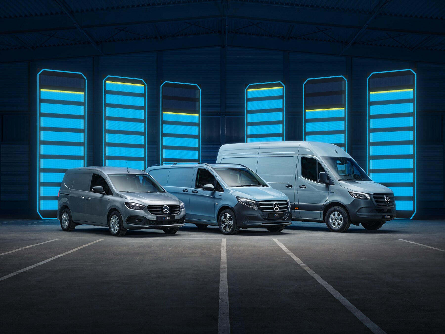 Una serie de furgonetas eléctricas de Mercedes-Benz se muestra en un depósito futurista con barras de recarga iluminadas