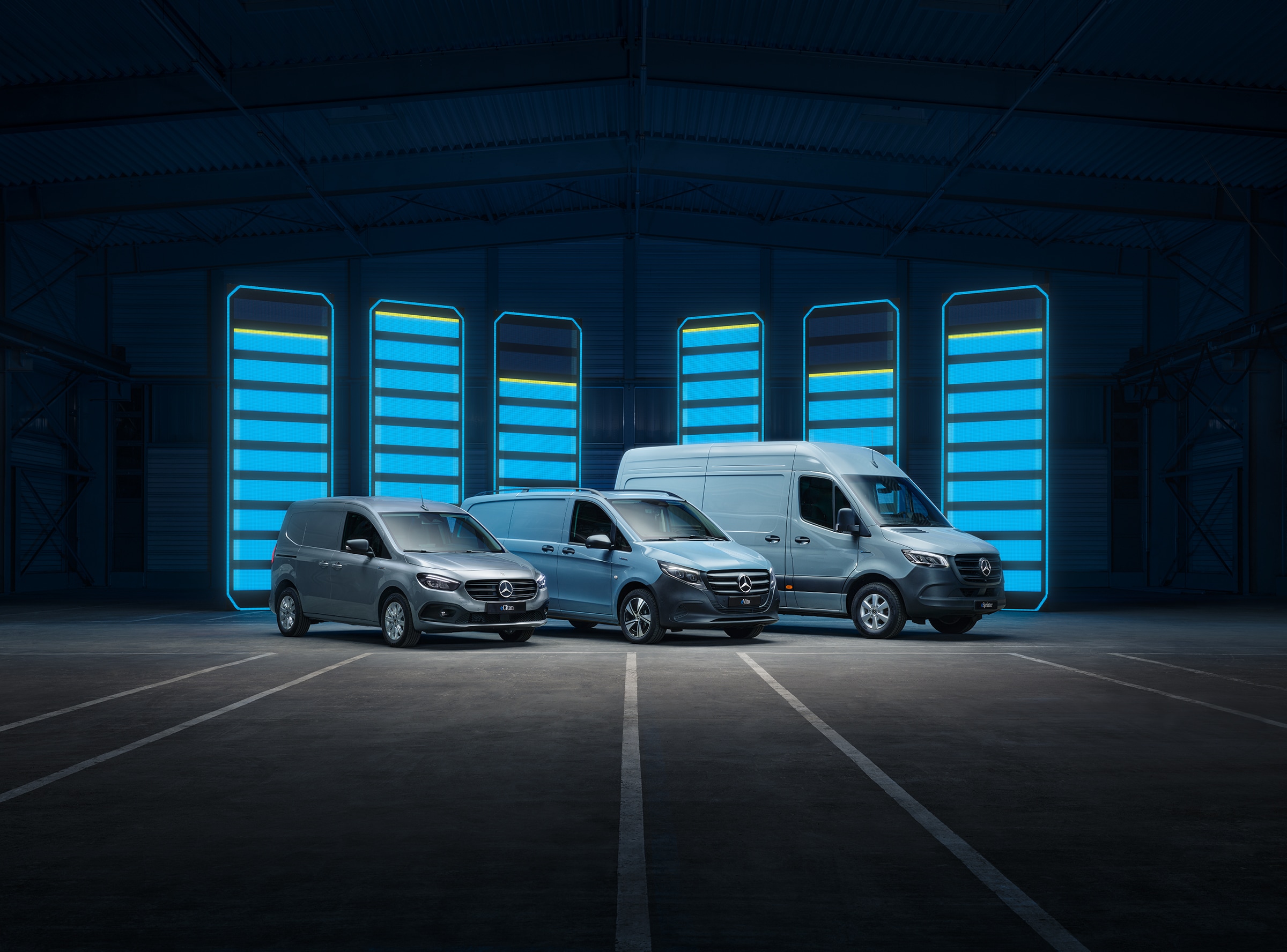 Gama de furgonetas eléctricas de Mercedes-Benz | Historia de los vehículos industriales | Mercedes-Benz Una serie de furgonetas eléctricas de Mercedes-Benz se muestra en un depósito futurista con barras de recarga iluminadas