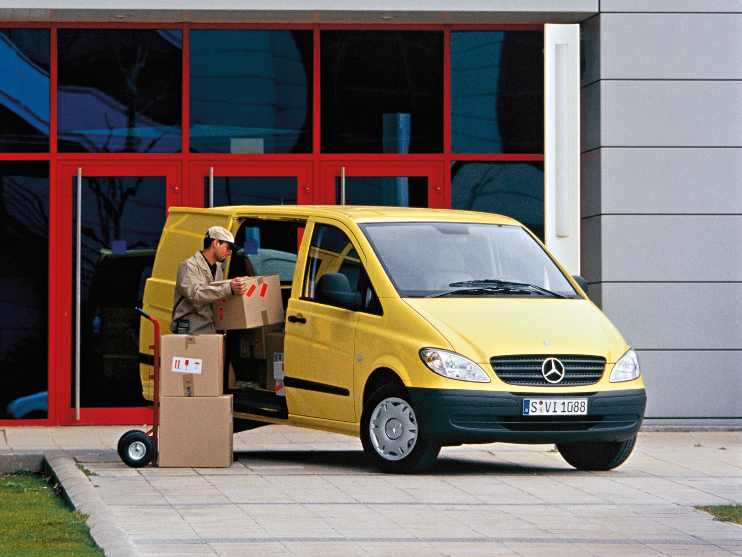 Una Mercedes-Benz Vito amarillo aparcado frente a un edificio, con un trabajador descargando paquetes