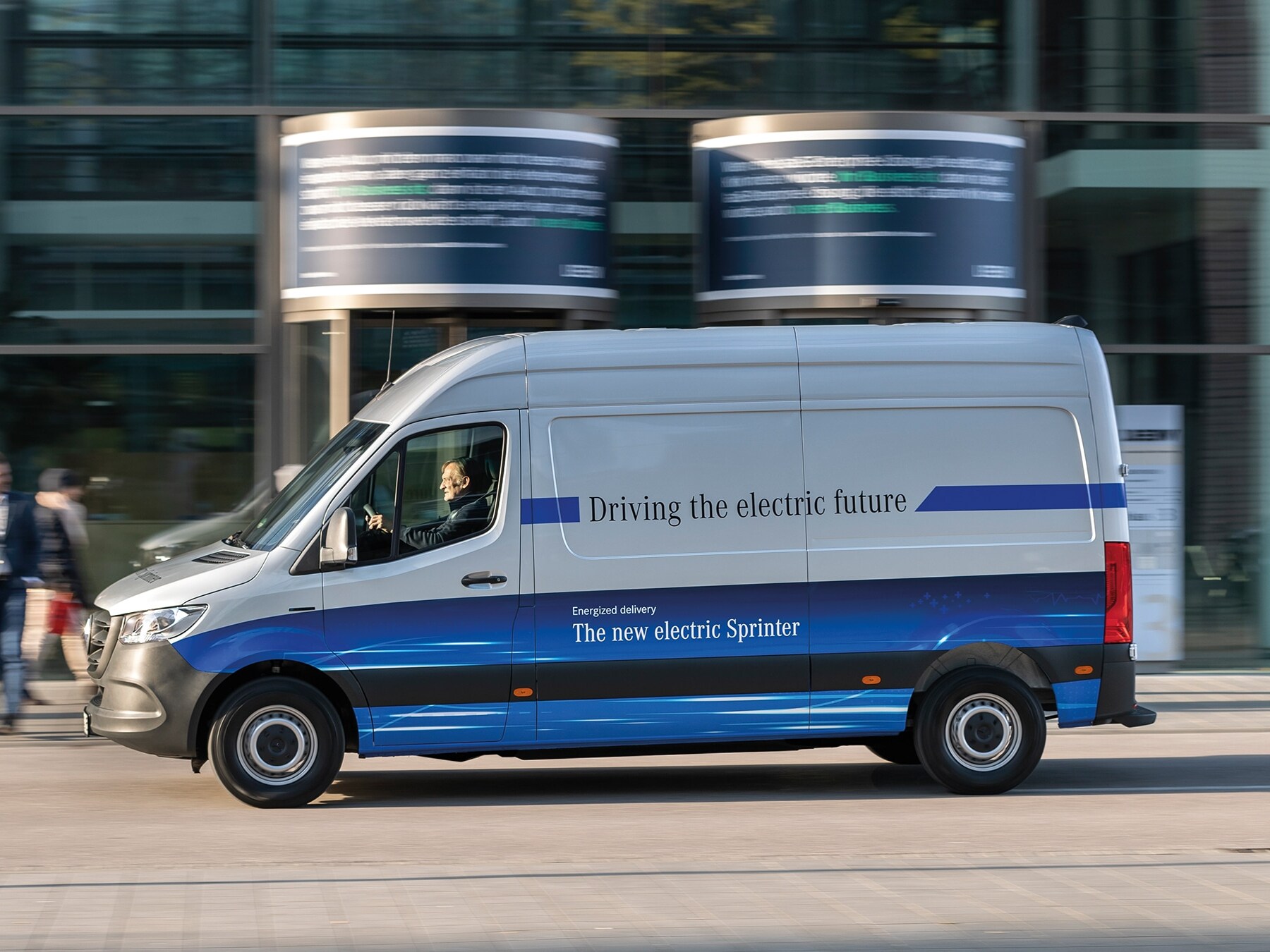 Furgoneta de reparto Mercedes-Benz eSprinter Panel Van circulando por una calle de una ciudad moderna