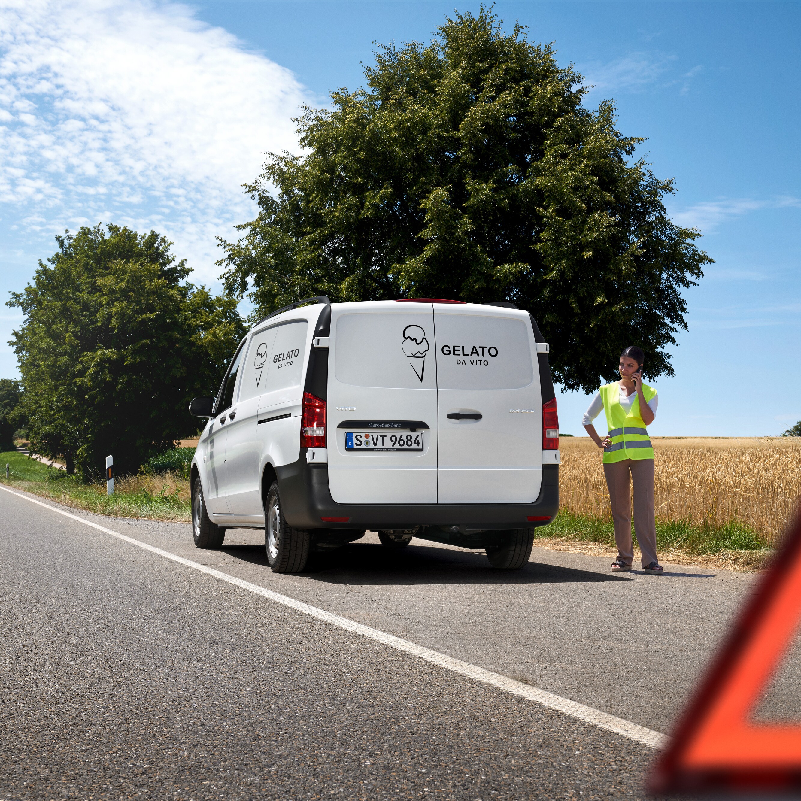 Una mujer llamando la línea directa de servicio Mercedes-Benz, un Mercedes-Benz Sprinter detenido al borde de un camino rural.