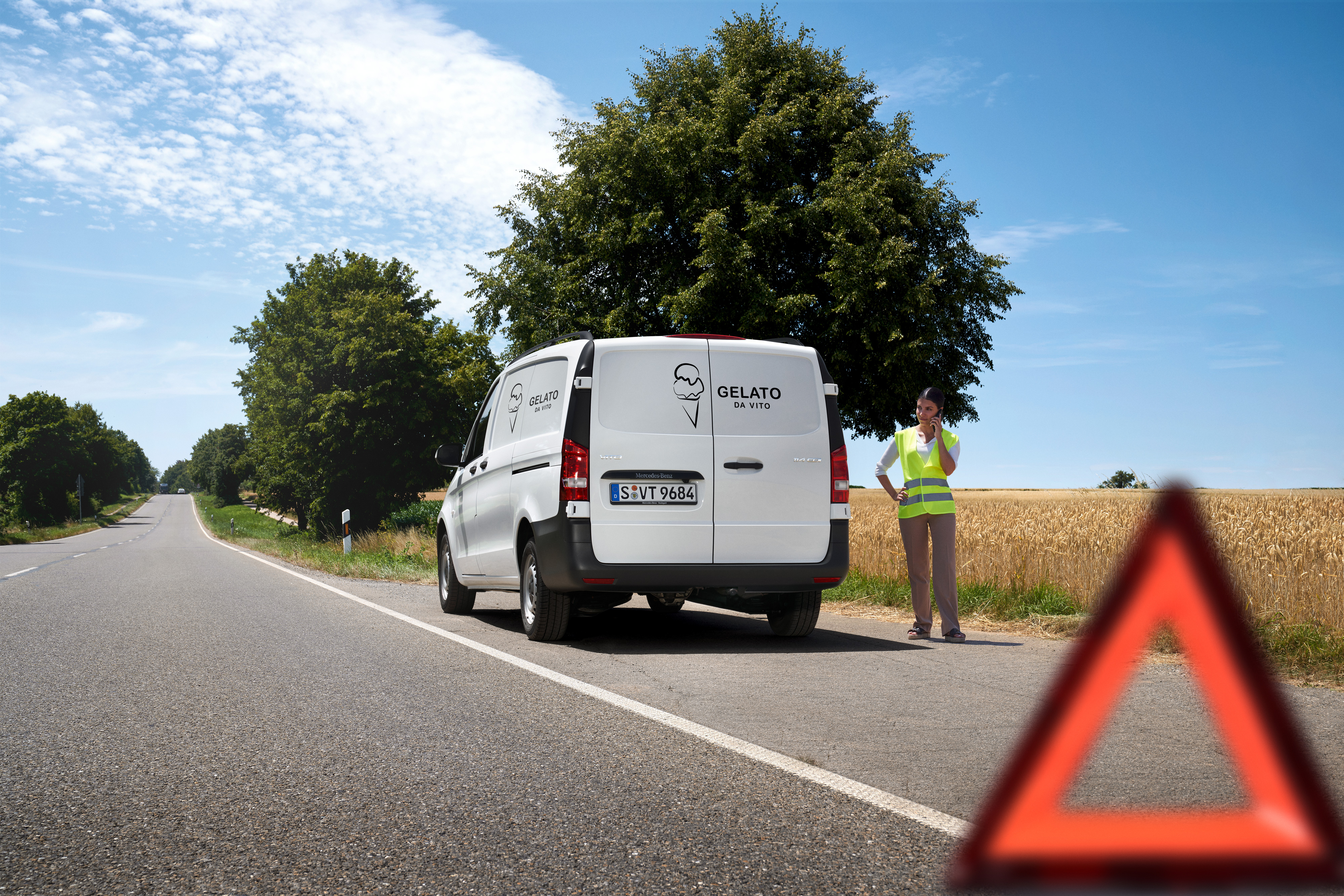 Mercedes-Benz | Cuidado de furgones | Service24h Una mujer llamando la línea directa de servicio Mercedes-Benz, un Mercedes-Benz Sprinter detenido al borde de un camino rural.