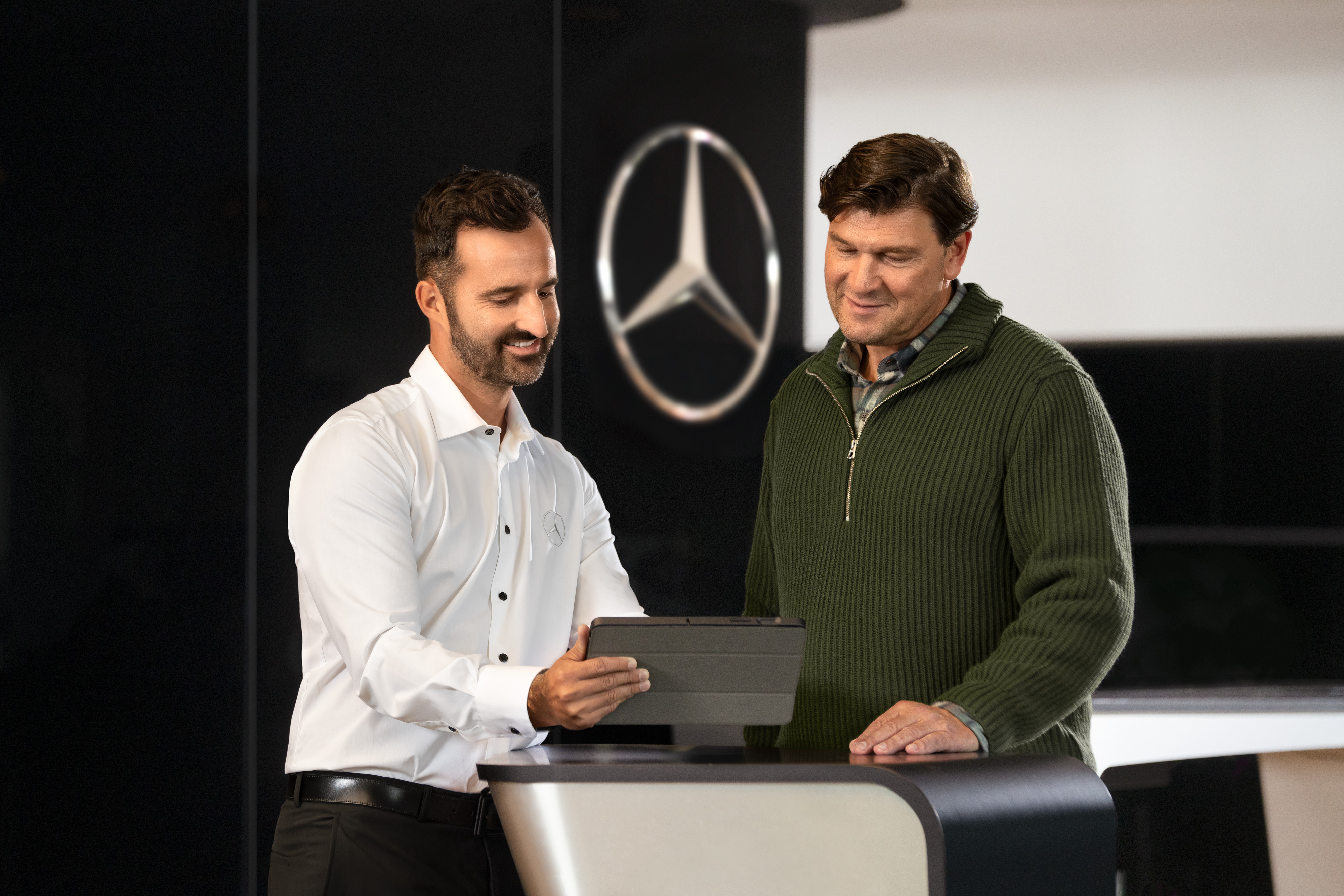 Mercedes-Benz | Cuidado de furgones | Apoyo individual Un empleado de Mercedes asesorando a los clientes en el mostrador con una tablet: asistencia individual y asesoramiento comercial en el concesionario.