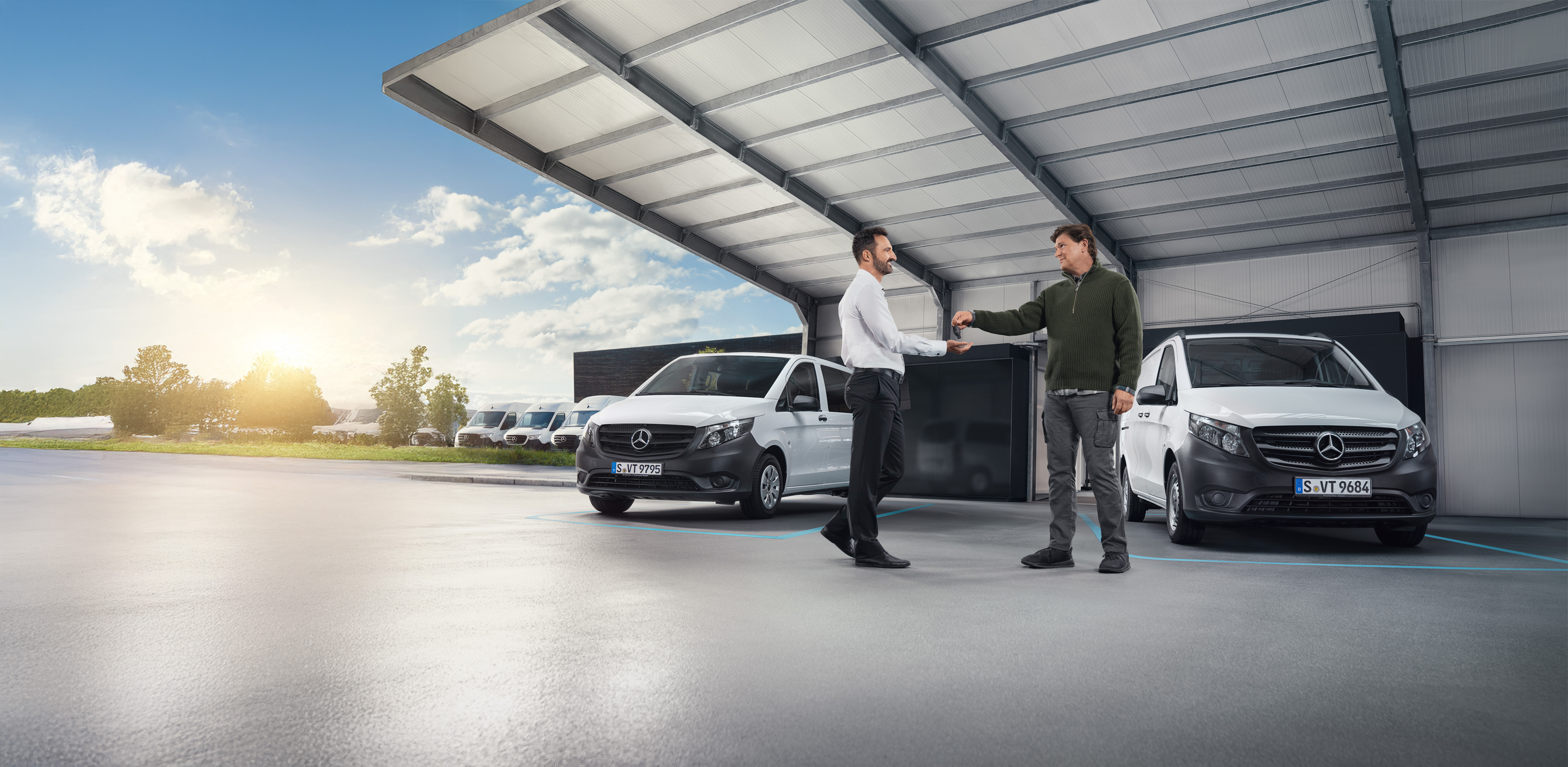 Mercedes-Benz | Cuidado de furgones | Apoyo individual Dos hombres conversando delante de una serie de furgones Mercedes-Benz blancos en una sala.