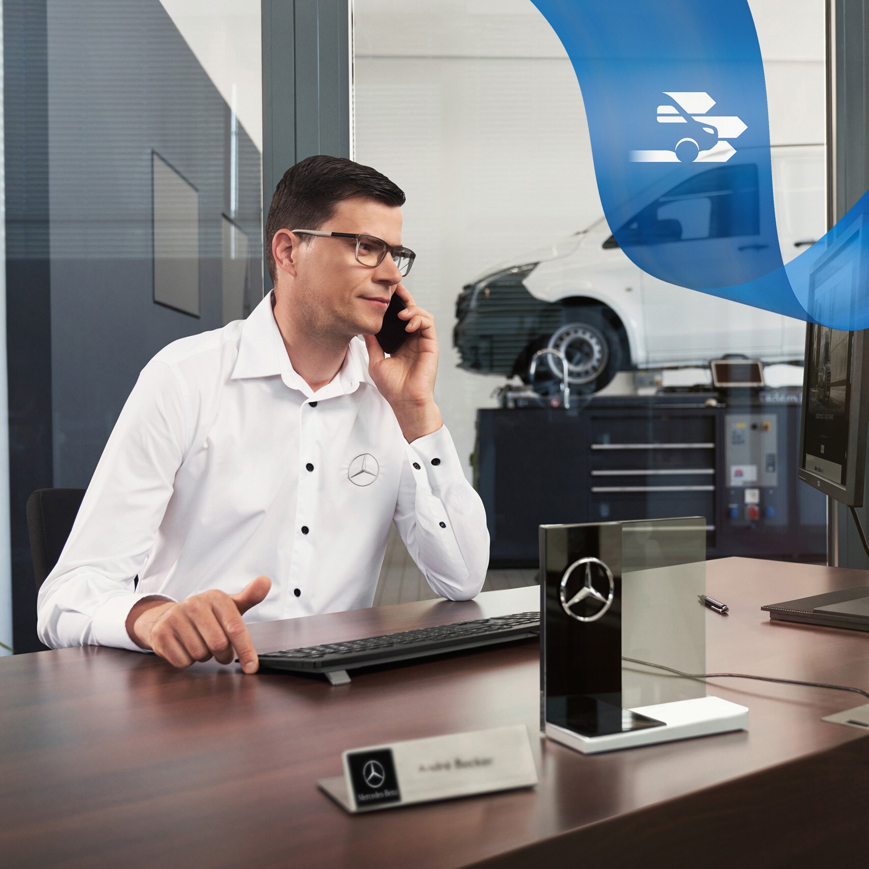 Un empleado en un mostrador hablando por teléfono con un furgón Mercedes-Benz Vito en el taller en el fondo.