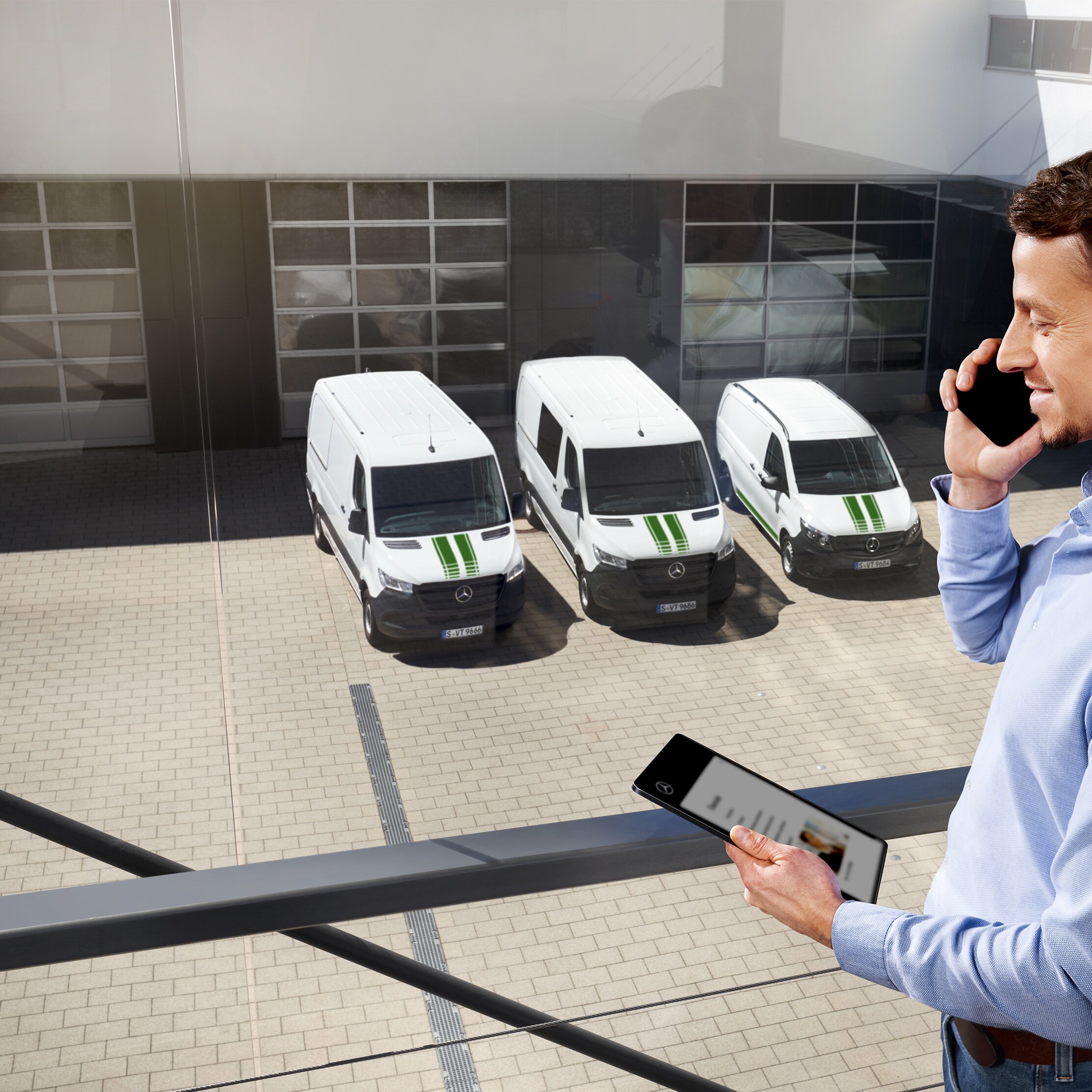 Cliente al teléfono delante de una flota de furgones blancas Mercedes-Benz.