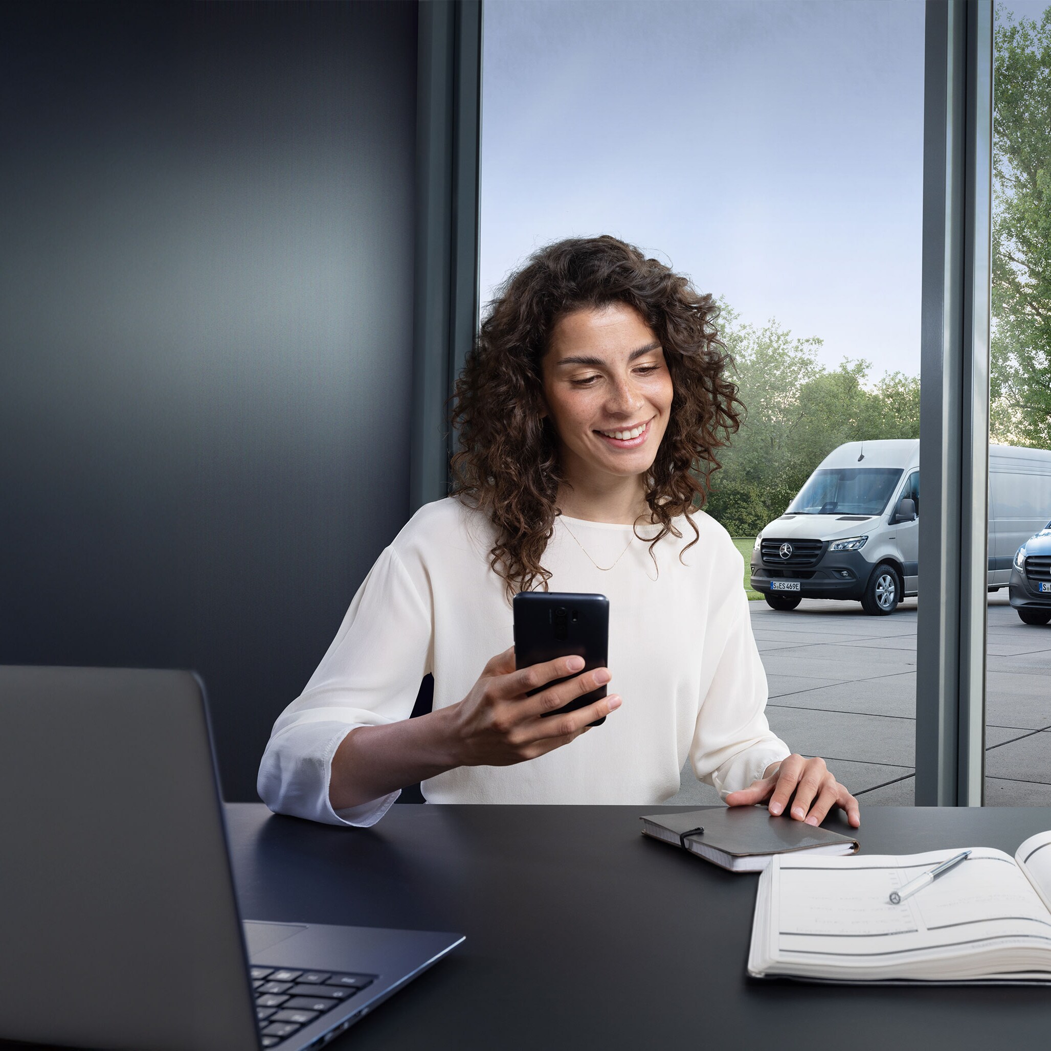 Mujer buscando un Servicio Oficial Mercedes-Benz en su smartphone con una serie de furgones Mercedes-Benz de fondo.