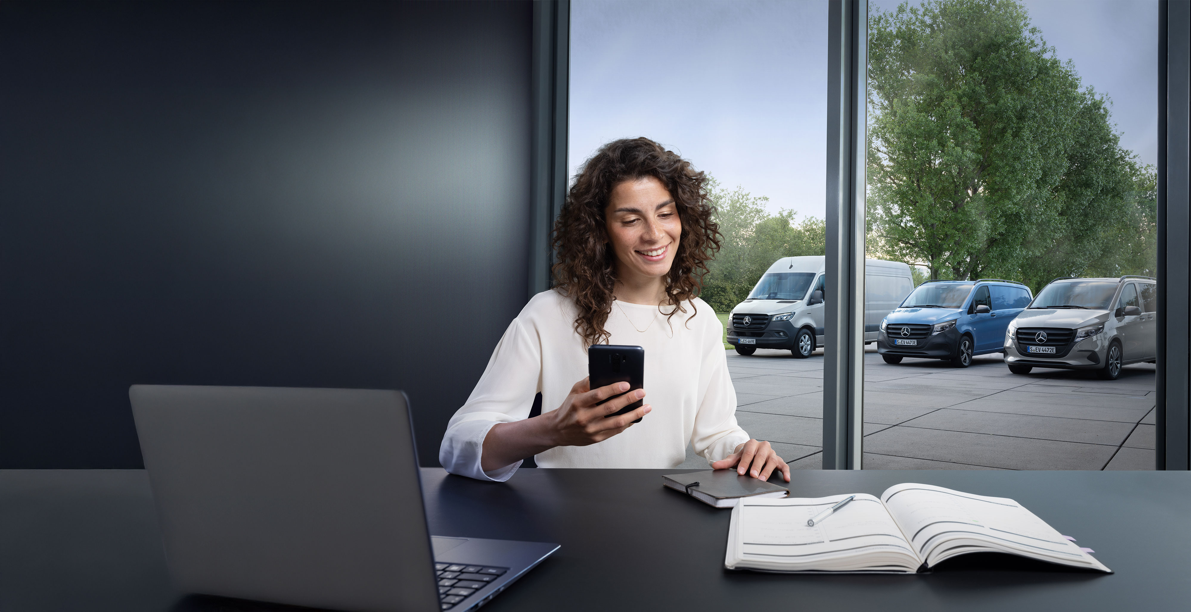 Mercedes-Benz | Conveniencia | Concesionario Oficial Mujer buscando un Servicio Oficial Mercedes-Benz en su smartphone con una serie de furgones Mercedes-Benz de fondo.