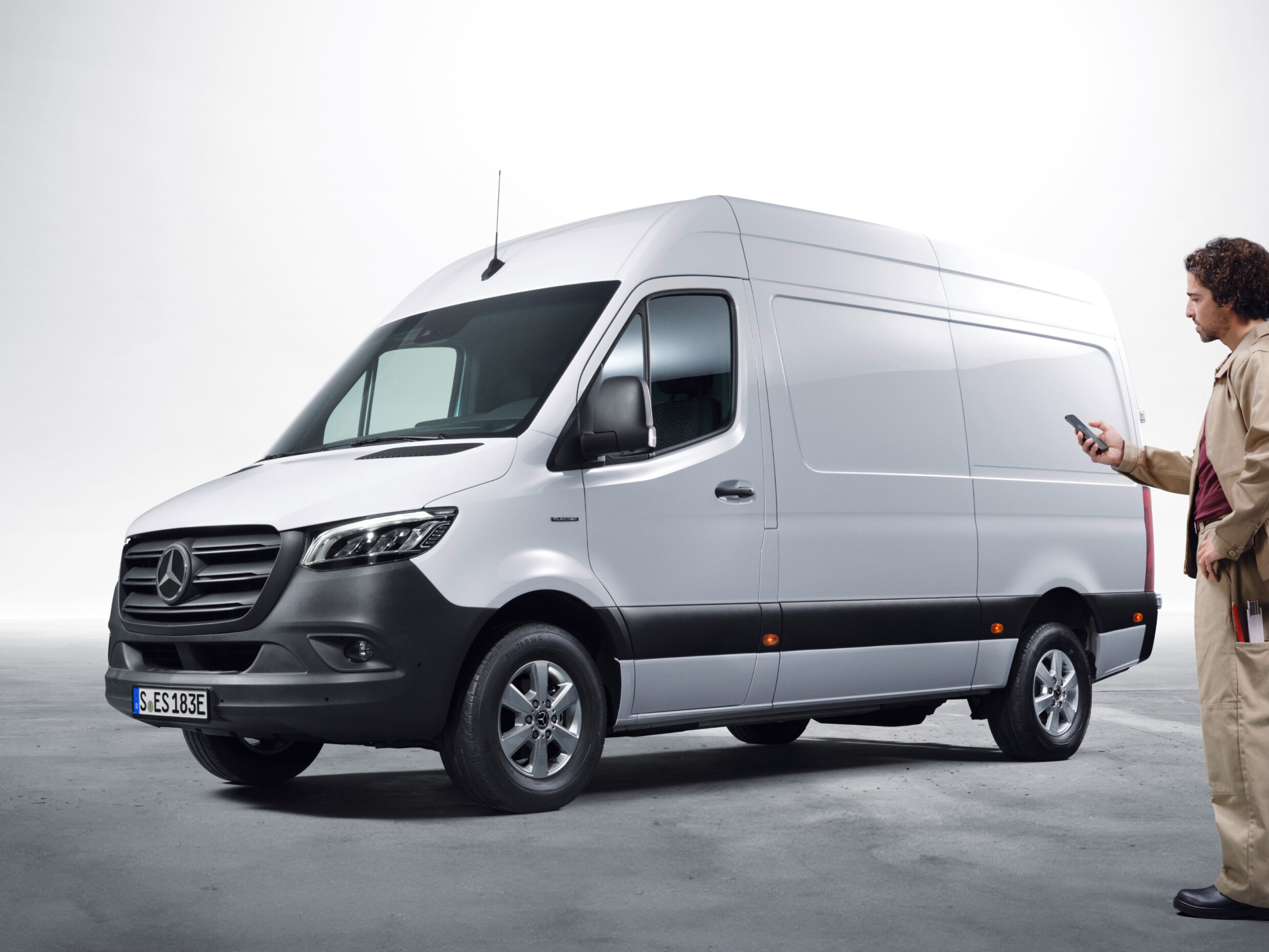 Mercedes-Benz Sprinter estacionada junto a una profesional que la gestiona desde su smartphone, destacando la conectividad y los servicios digitales para vehículos comerciales.