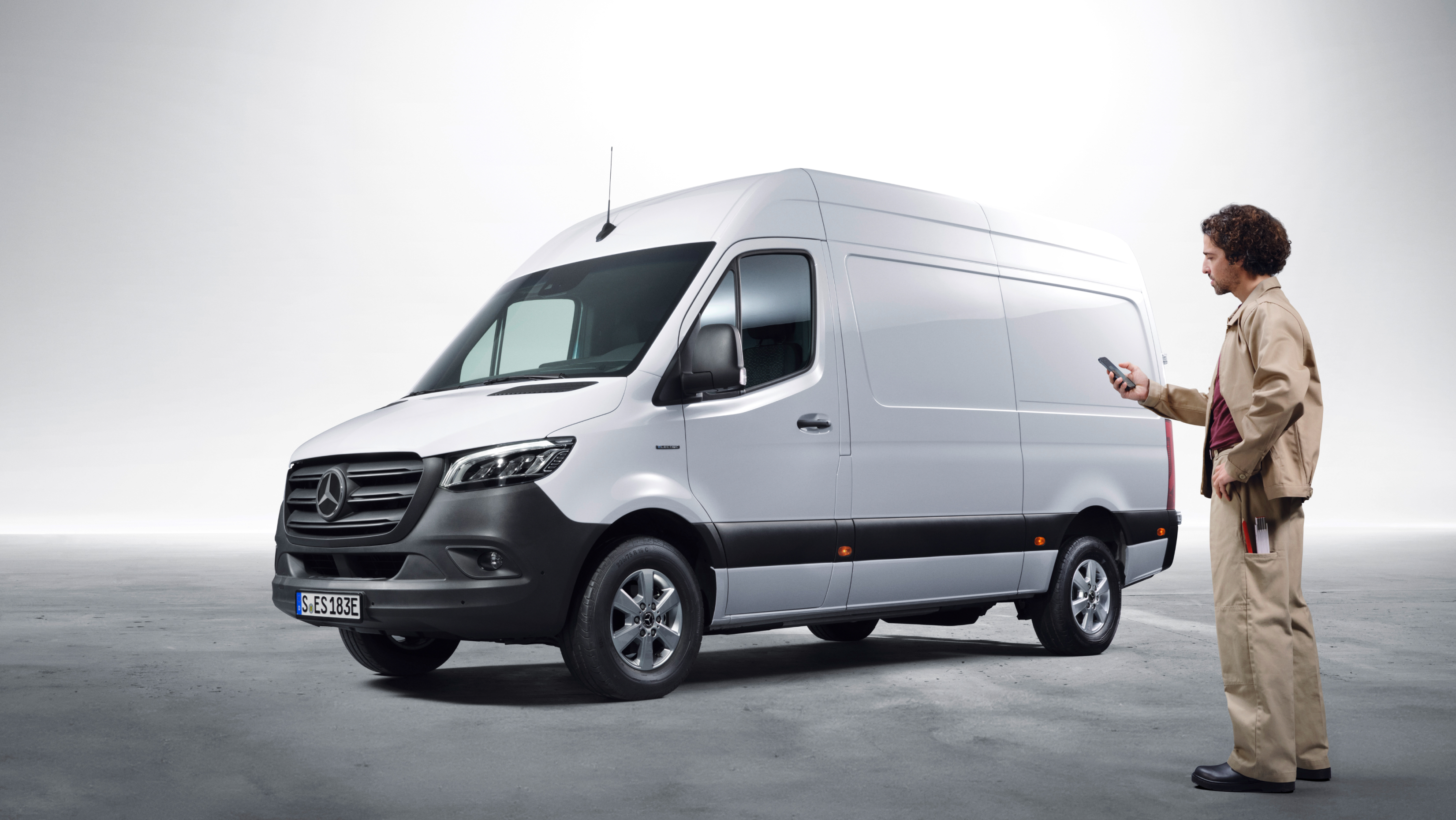 Extras digitales | Mercedes-Benz Vans Mercedes-Benz Sprinter estacionada junto a una profesional que la gestiona desde su smartphone, destacando la conectividad y los servicios digitales para vehículos comerciales.