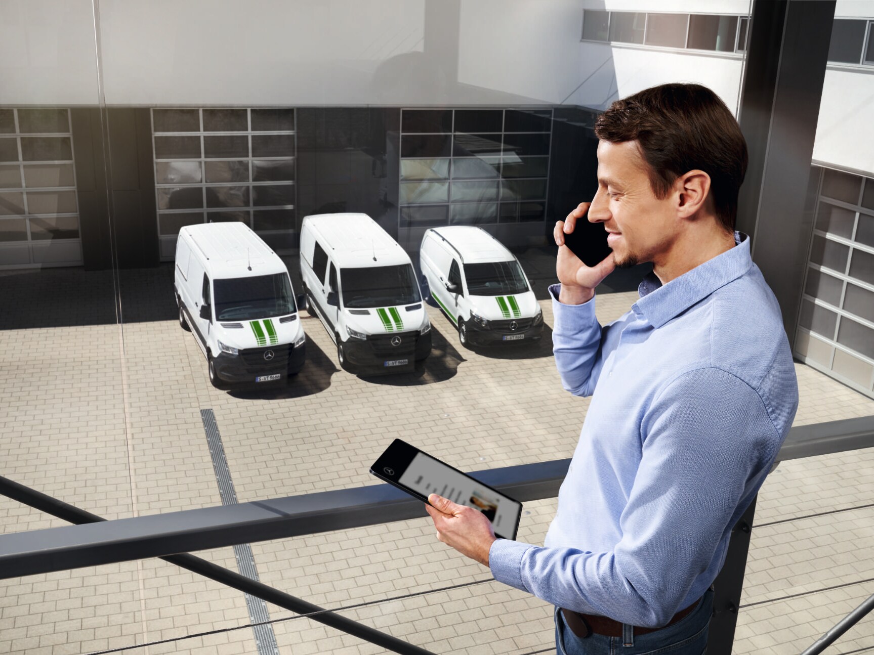 A Mercedes-Benz consultant standing with a phone and a tablet in the hand with Mercedes-Benz Transporters in the background.