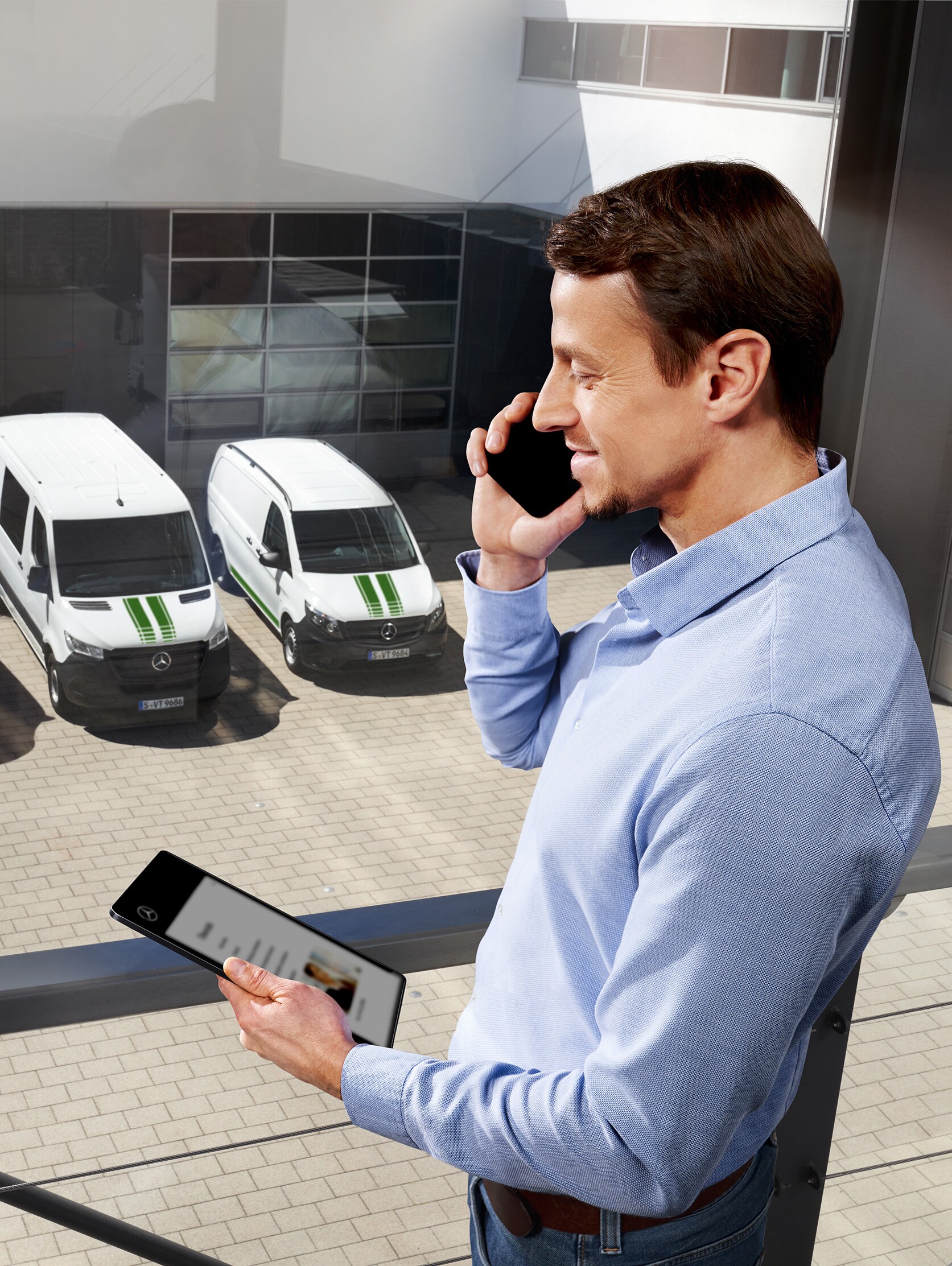 Hombre hablando por teléfono con tablet delante de tres furgones Mercedes-Benz, tema: ¿cuál es la duración de la garantía del fabricante en Mercedes-Benz?