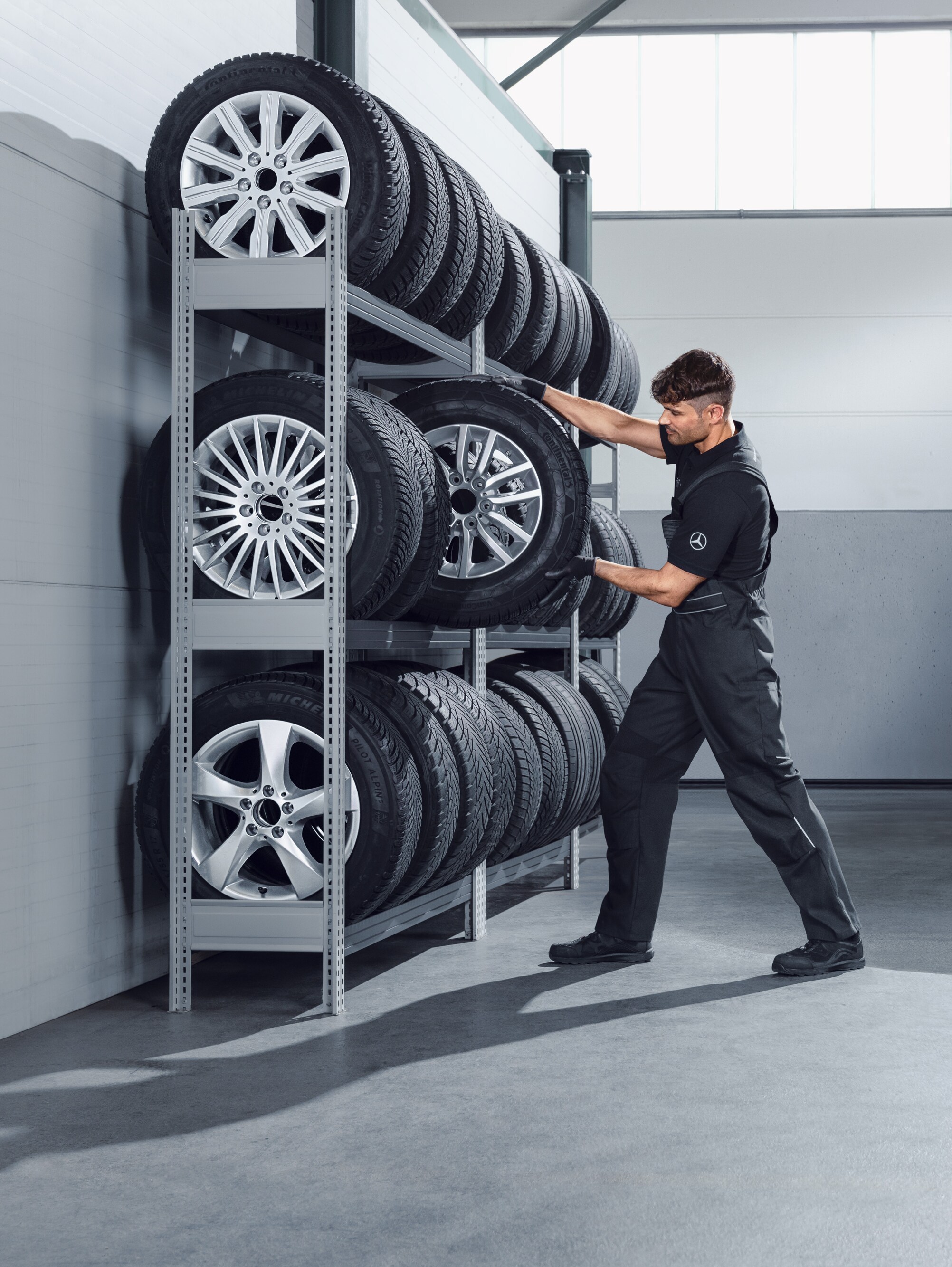 Mecánico eligiendo, de la estantería del taller, ruedas Mercedes-Benz de invierno completas para una Sprinter blanca.