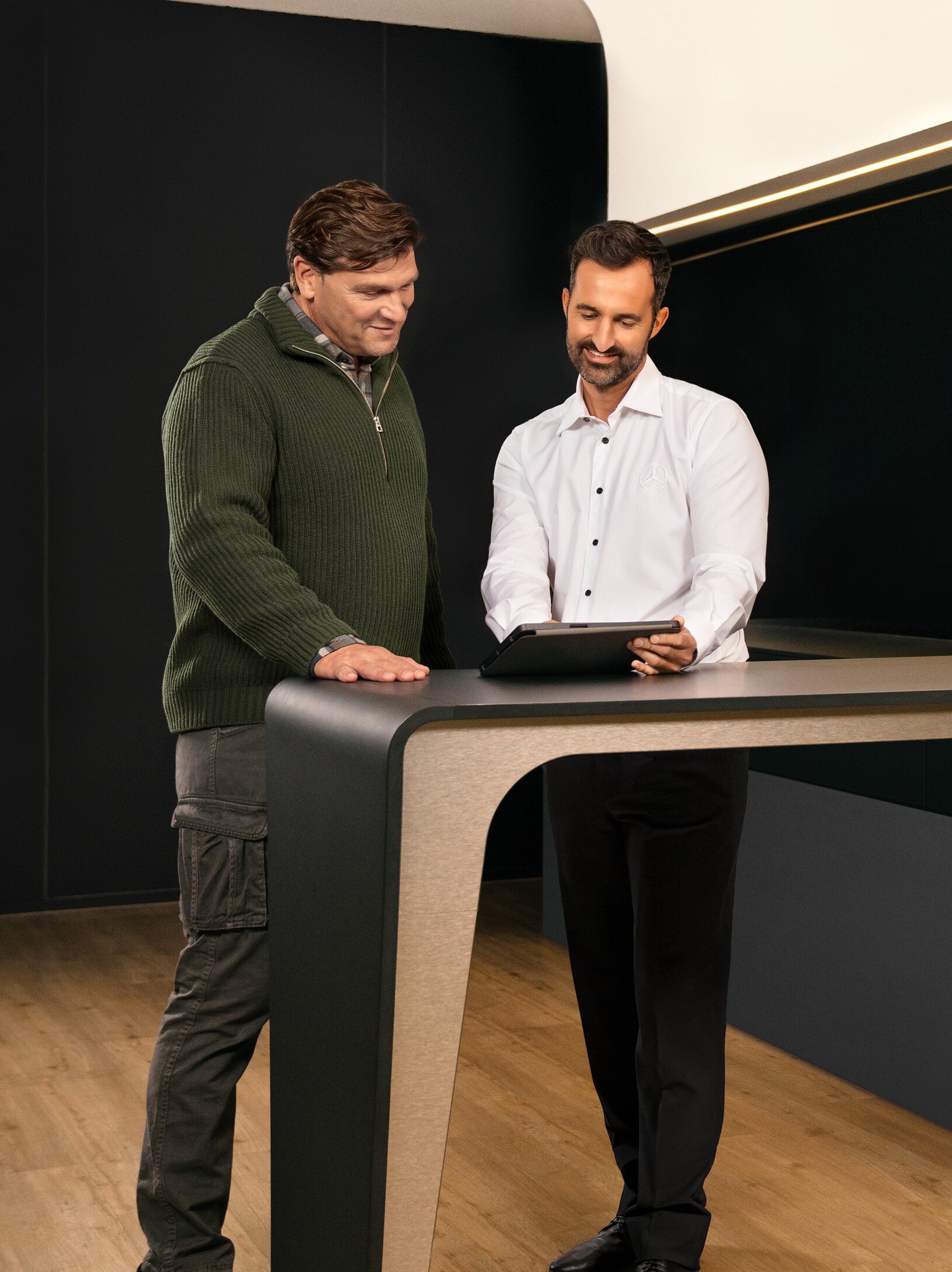 Dos hombres en una consulta alrededor de una mesa mirando un iPad.