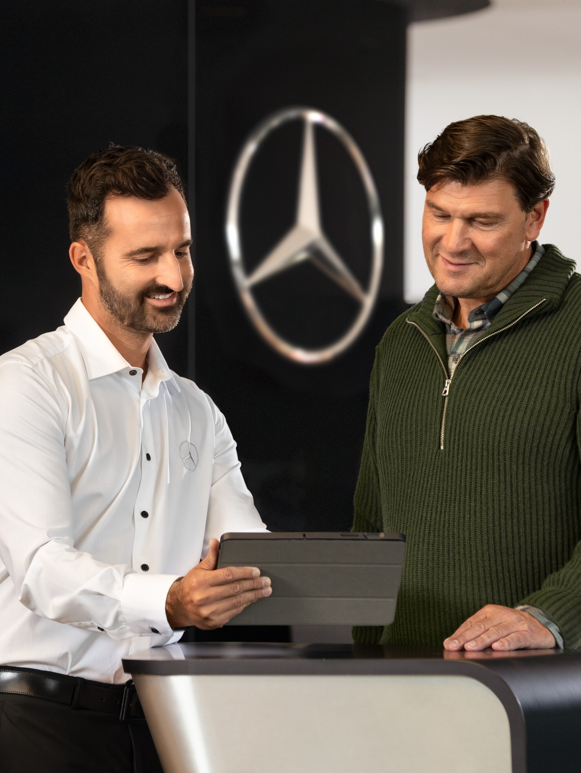 Dos hombres conversando en un mostrador y mirando una tablet, delante de la estrella de Mercedes-Benz.
