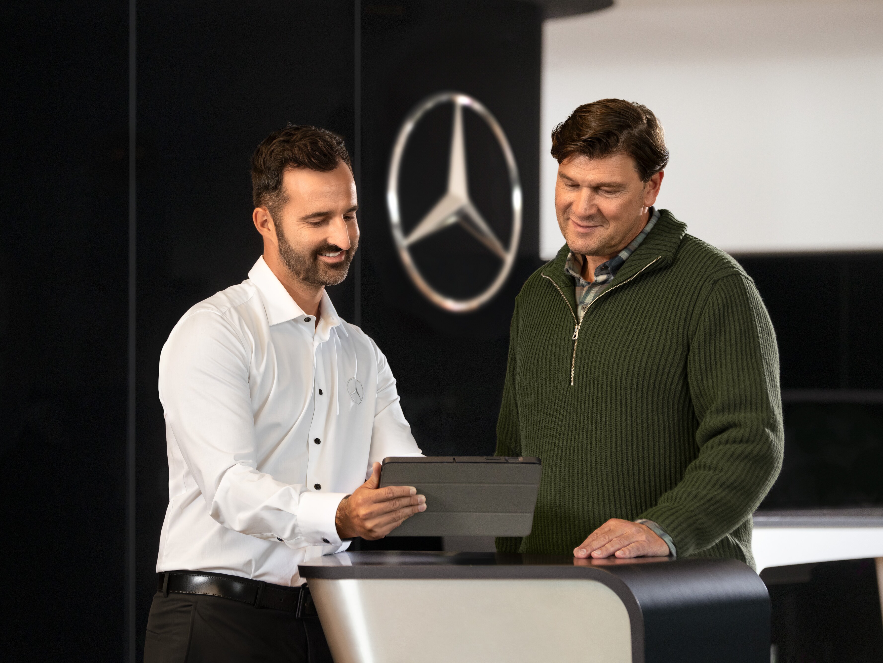 Dos hombres conversando en un mostrador y mirando una tablet, delante de la estrella de Mercedes-Benz.