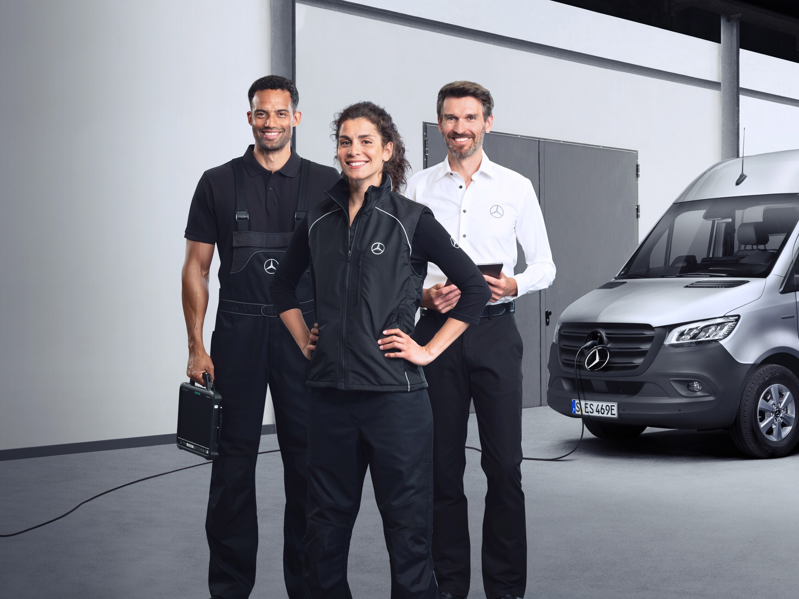 Tres empleados delante de un Mercedes-Benz eSprinter plateado con el cable de carga conectado.