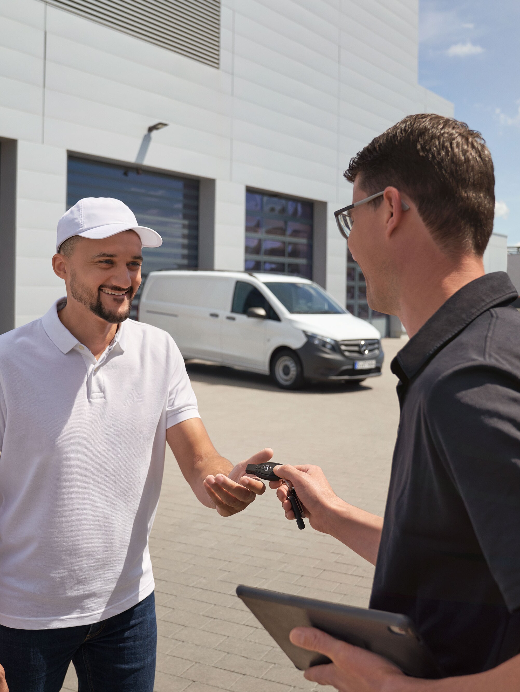 Un técnico entrega el llavero a un cliente con un furgón Mercedes-Benz Vito blanco al fondo.