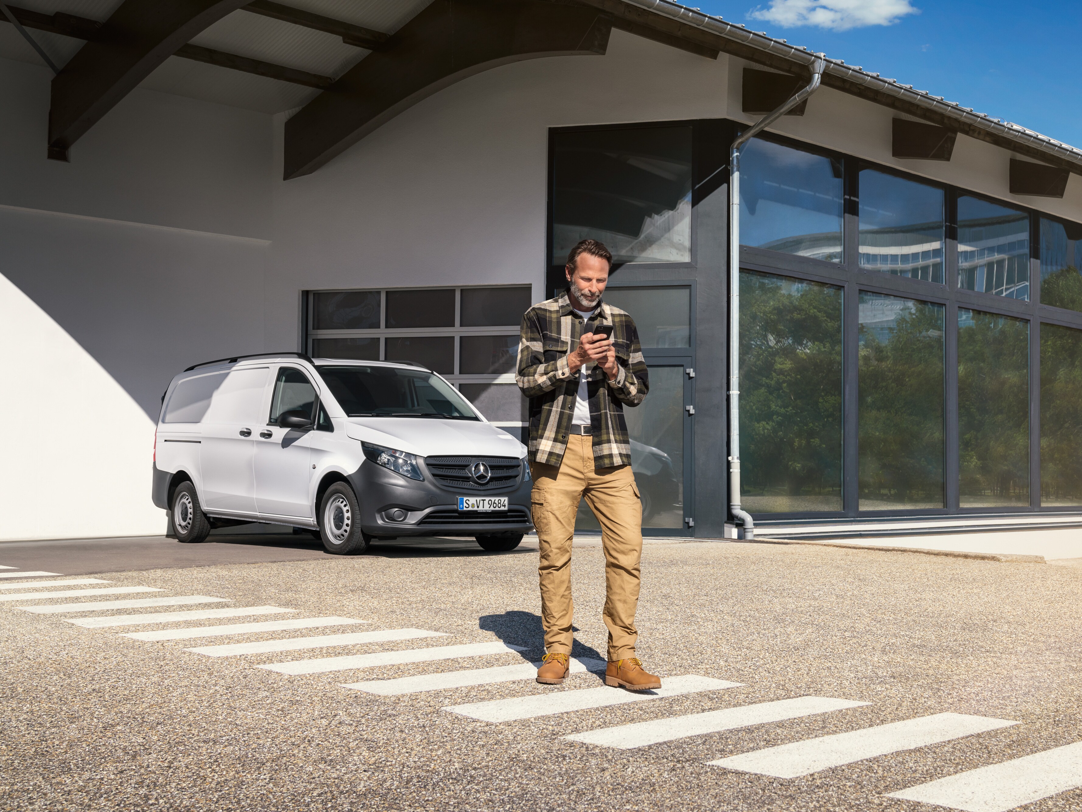 Un hombre delante de un furgón Mercedes-Benz Vito blanco utilizando su smartphone.
