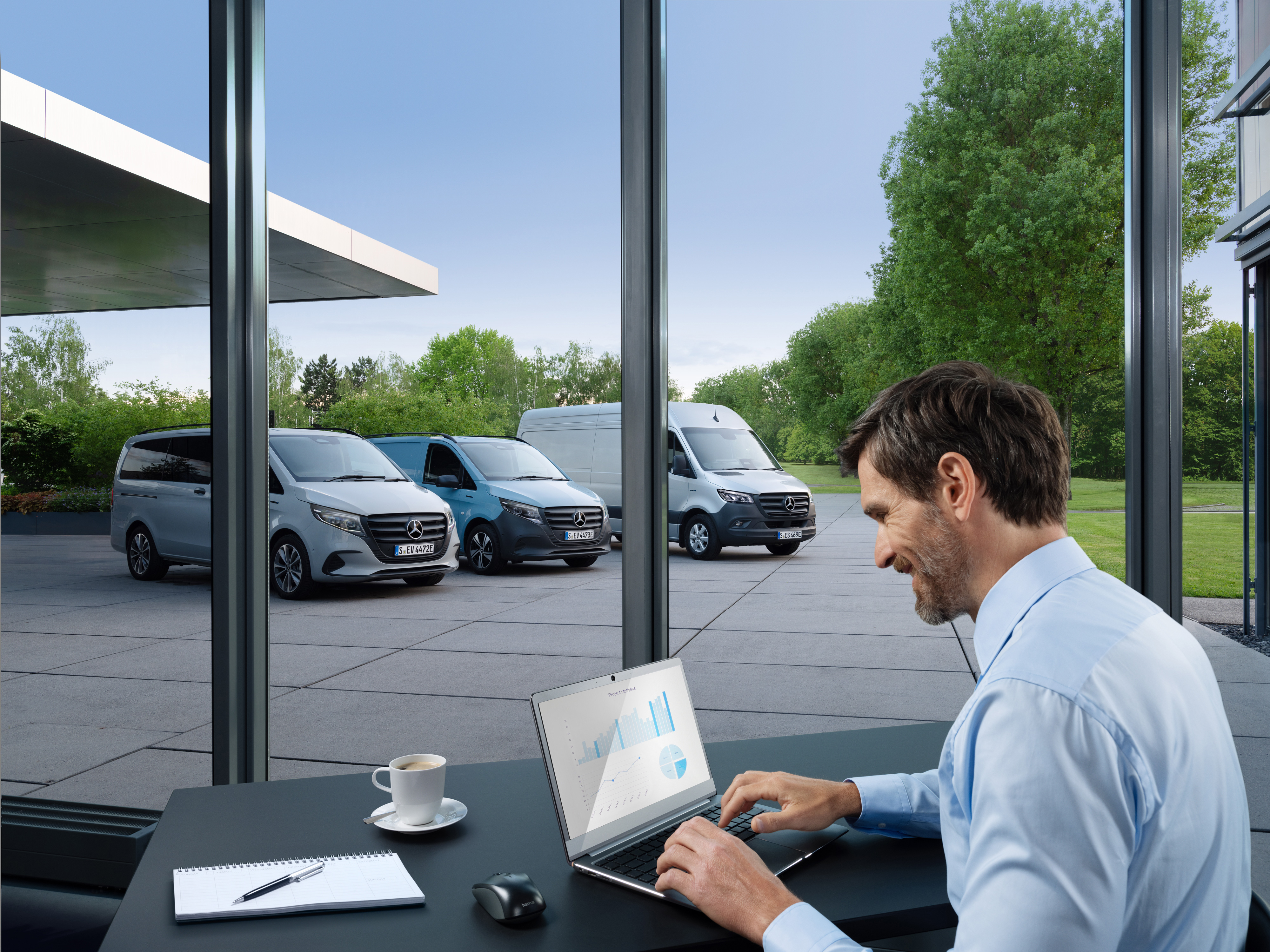 Mercedes-Benz | Servicio para vehículos eléctricos | Paquetes Un hombre trabajando con una laptop, afuera se ve una serie de furgones Mercedes-Benz.