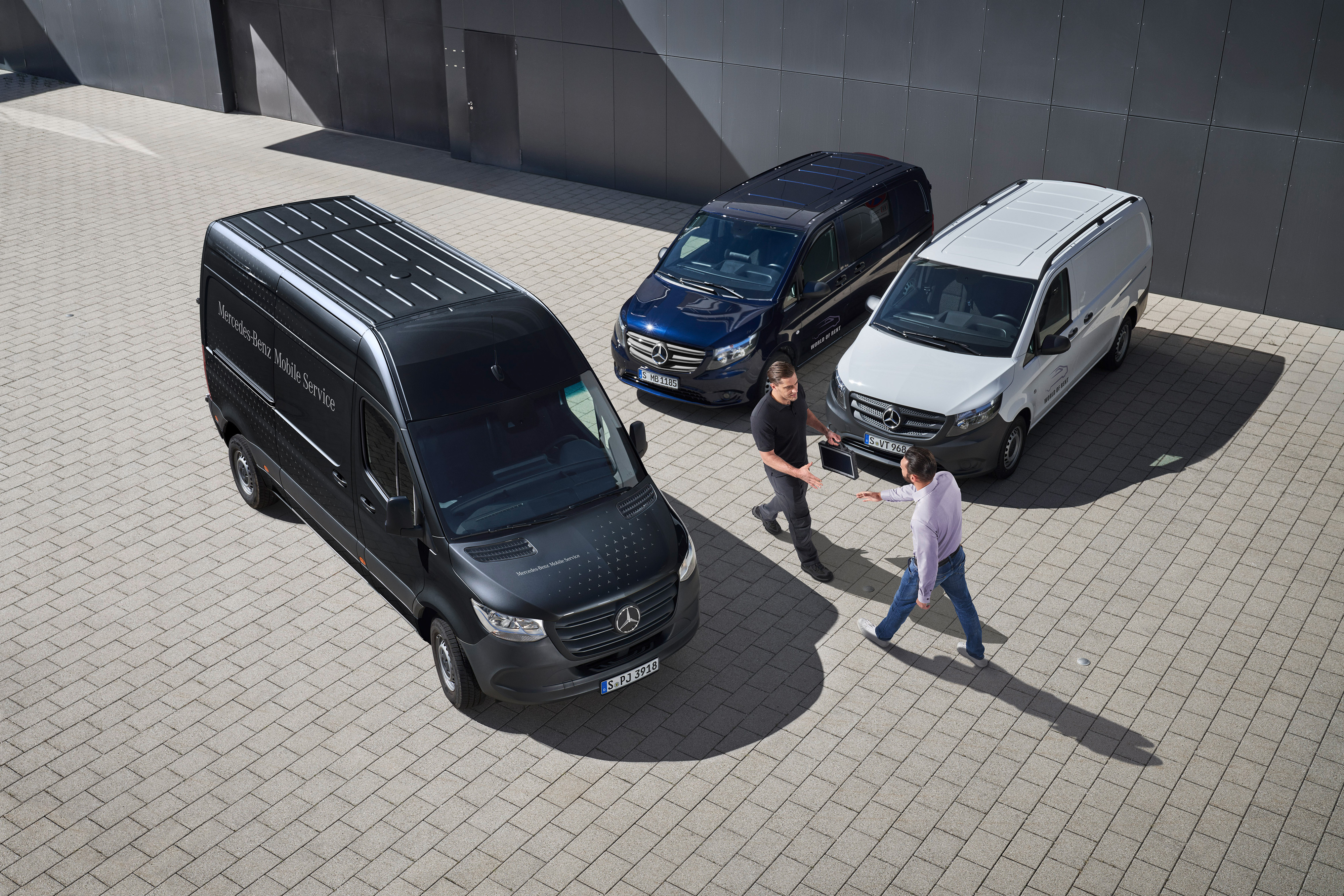 Mercedes-Benz | Servicios para flotas de furgones | Oficina de Enlace Técnico Un funcionario de enlace técnico de Mercedes-Benz saluda a un cliente en un aparcamiento caminando entre tres furgones Mercedes-Benz.