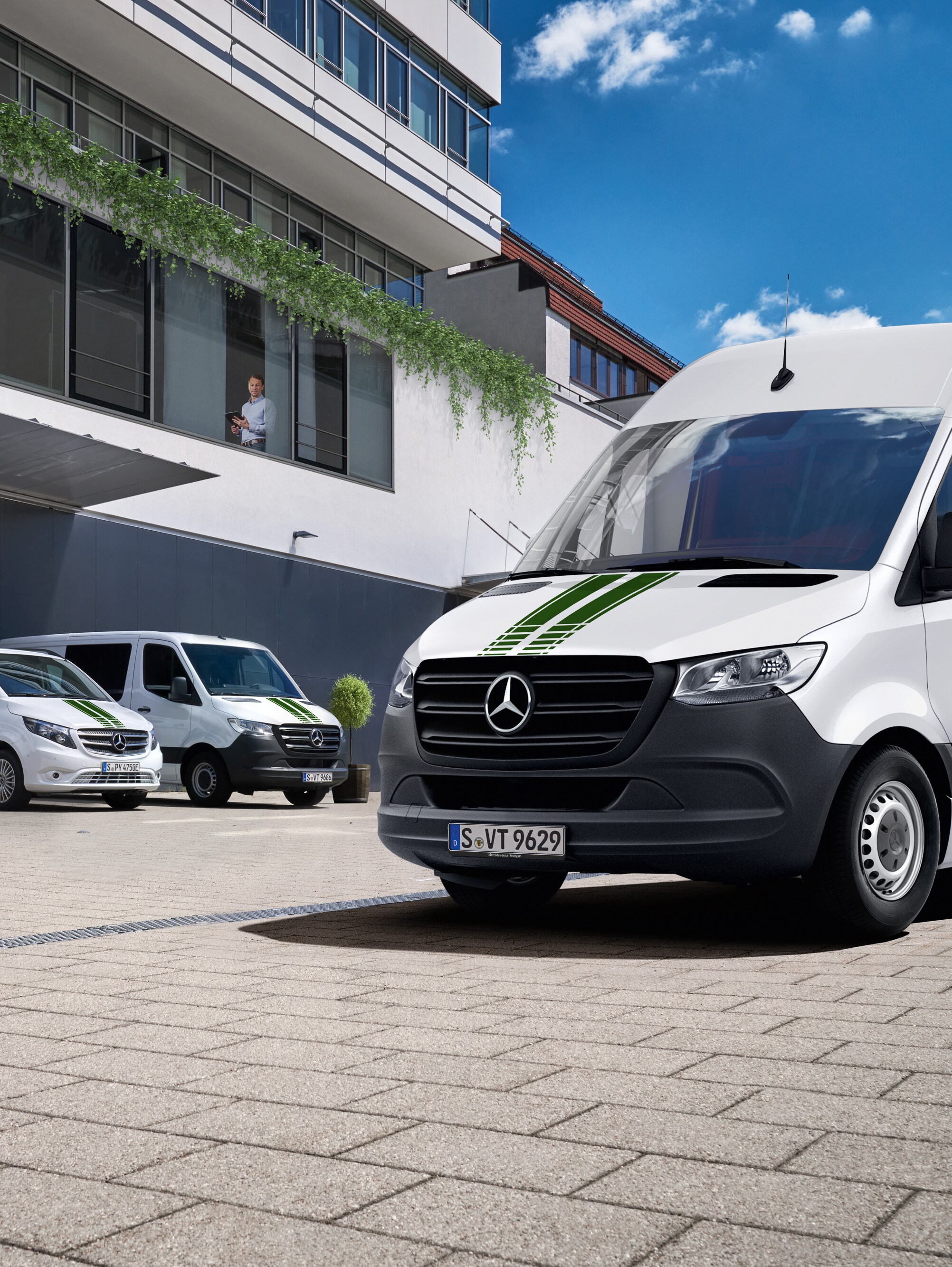Una flota de furgones blancos Mercedes-Benz frente a un edificio de oficinas en un día soleado con cielo azul.